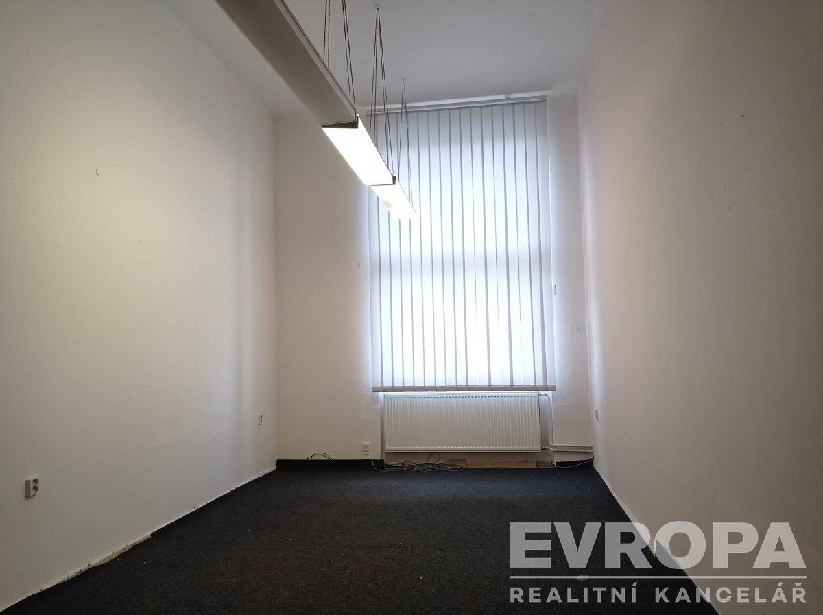 Prázdná kancelář s velkým oknem, moderní zářivkové osvětlení, neutrální koberec, ideální pro rekonstrukci nebo přizpůsobení.