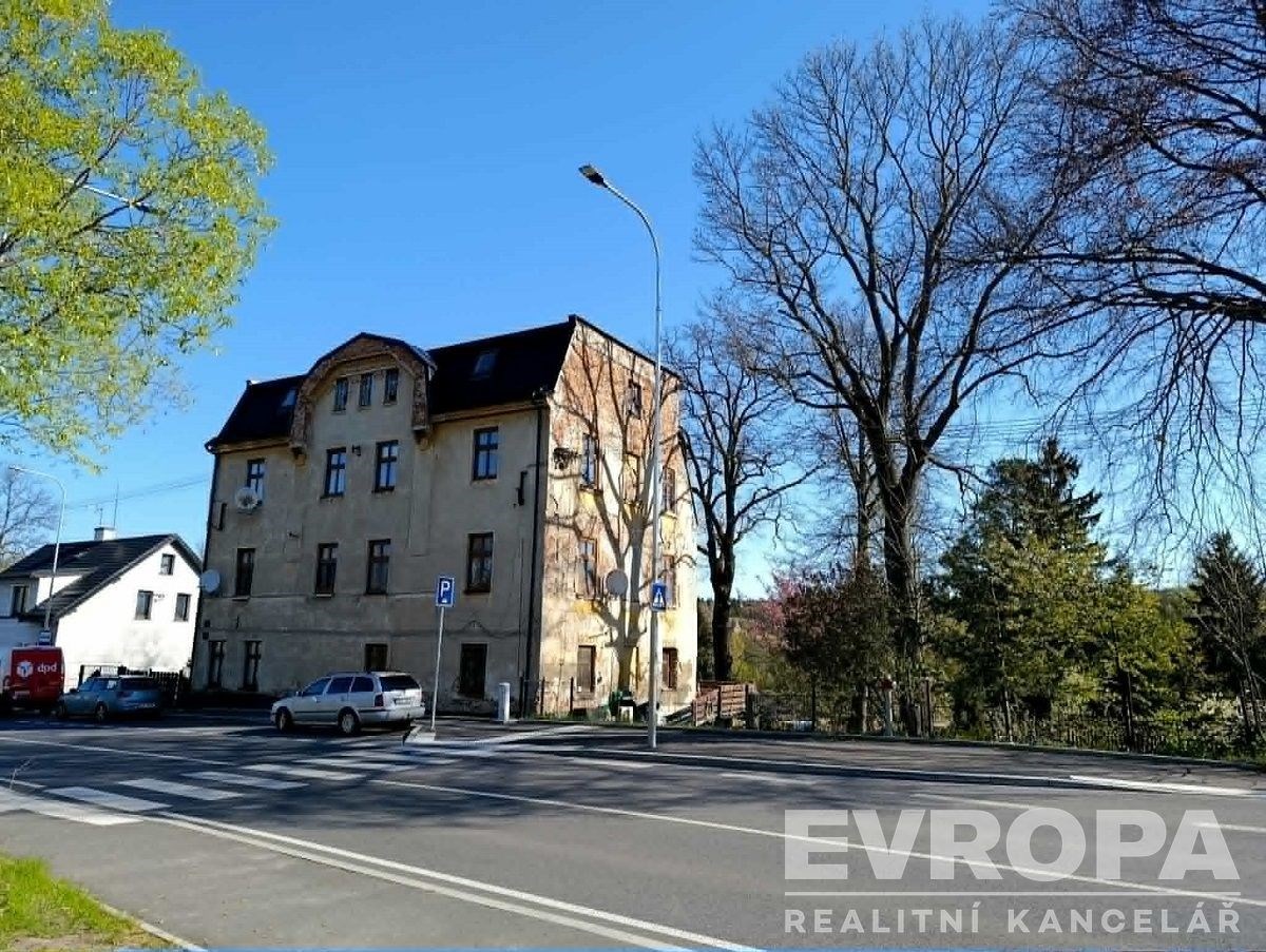 Starší bytový dům s historickou fasádou, nacházející se na rohu rušné ulice, obklopený vzrostlými stromy a s parkovacími místy v okolí.