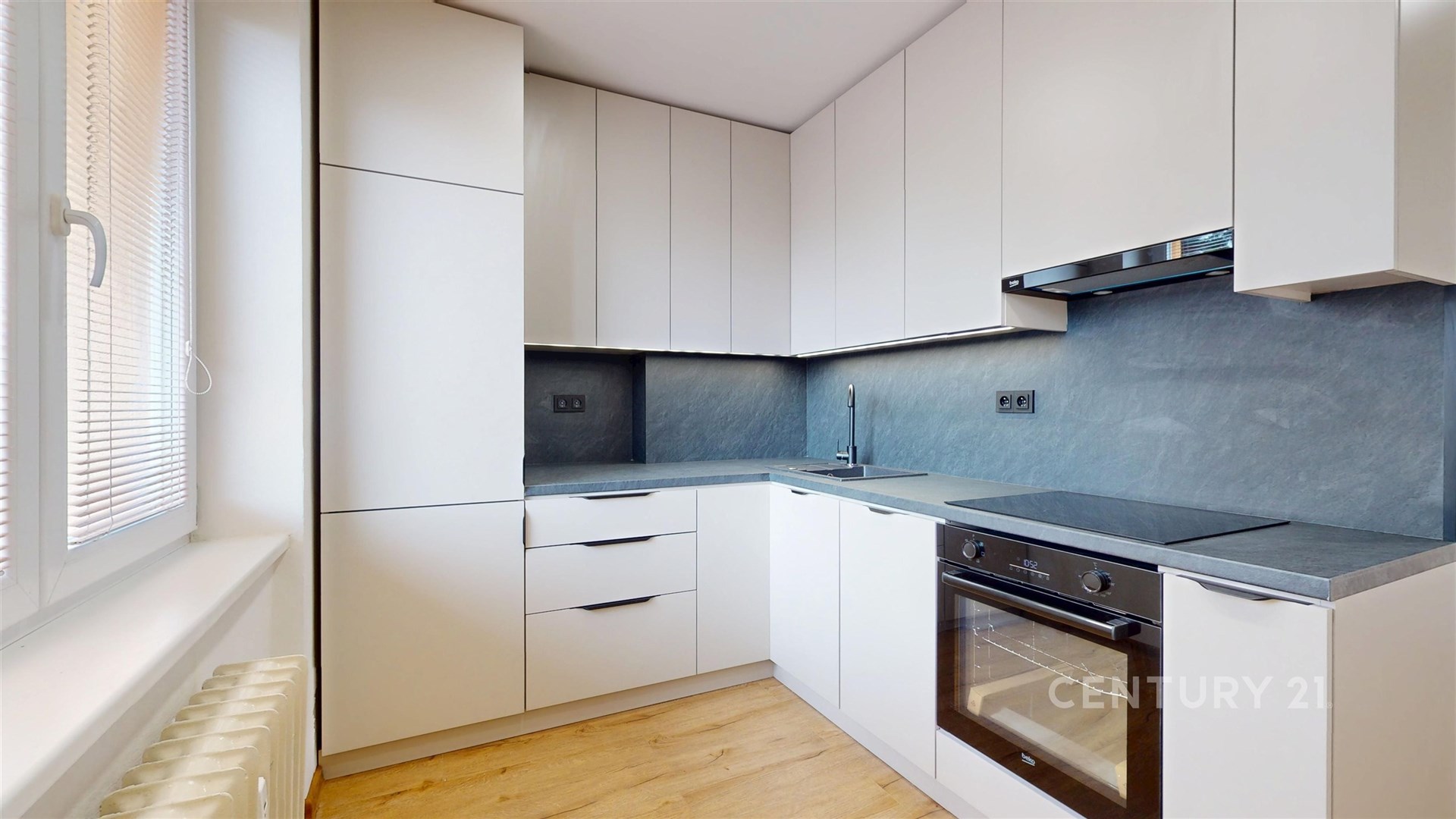 Moderní kuchyň s vestavěnými skříněmi a elektrospotřebiči, světlá dřevěná podlaha a elegantní tmavá pracovní deska