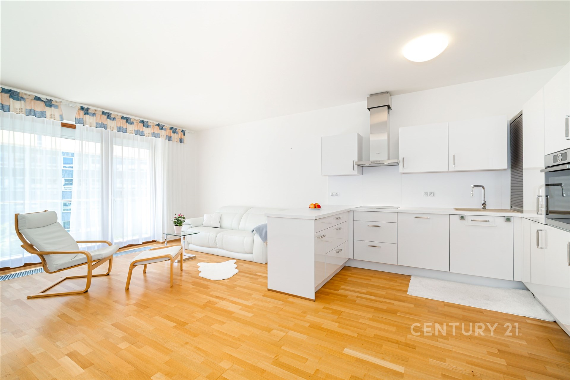 Světlý obývací pokoj s moderní kuchyní, parketová podlaha, velká okna, renovovaný interiér, bílý nábytek, otevřený prostor.