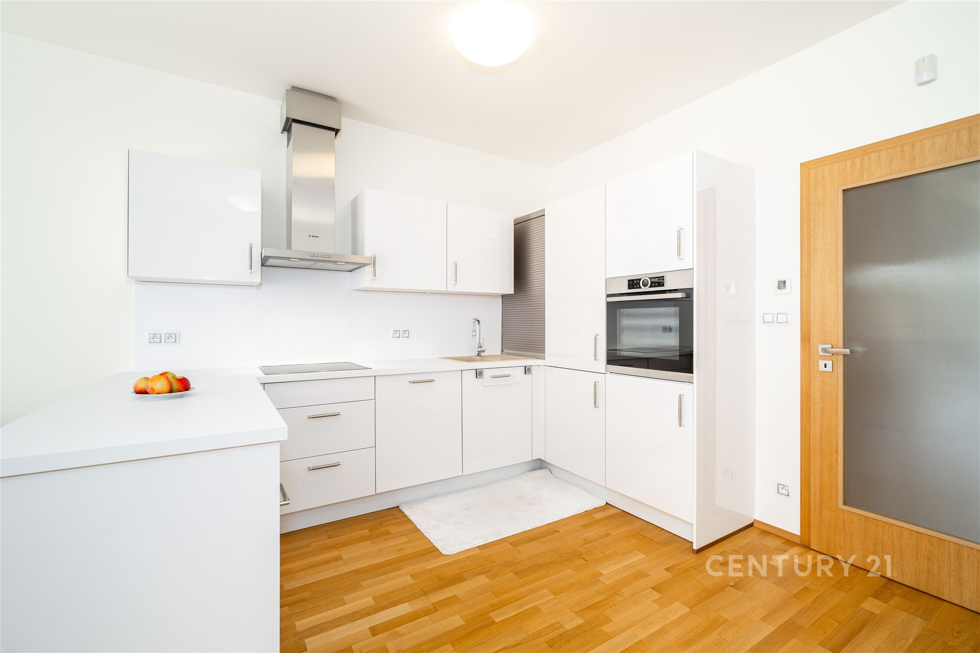 Moderní kuchyň s parketovou podlahou a vestavěnými spotřebiči, v bílém provedení. Světlý, elegantní design s dřevěnými doplňky.
