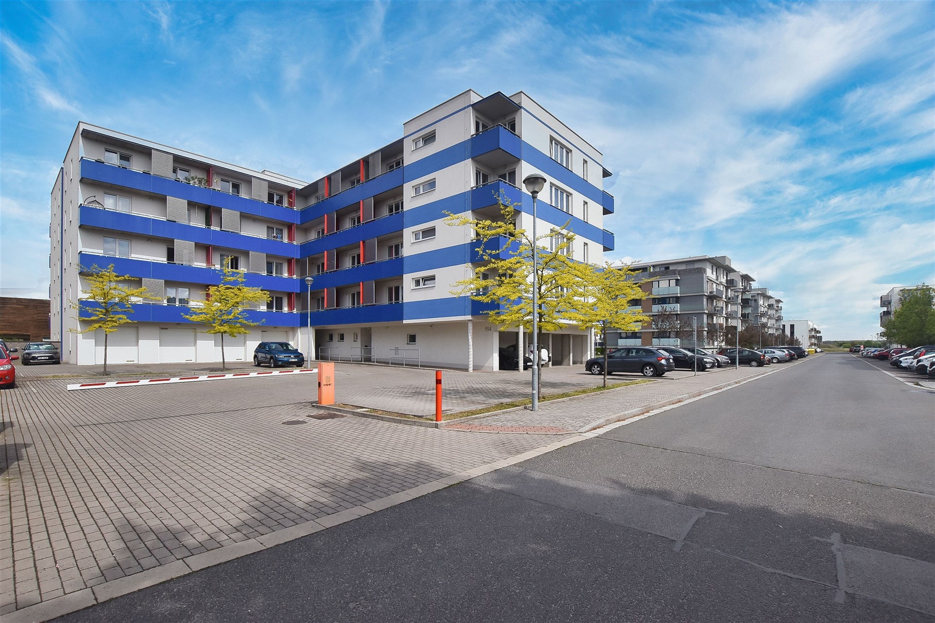 Moderní bytový dům se světlou fasádou a modrými balkony, k dispozici parkovací místa, vhodný pro rezidenční bydlení nebo investici.