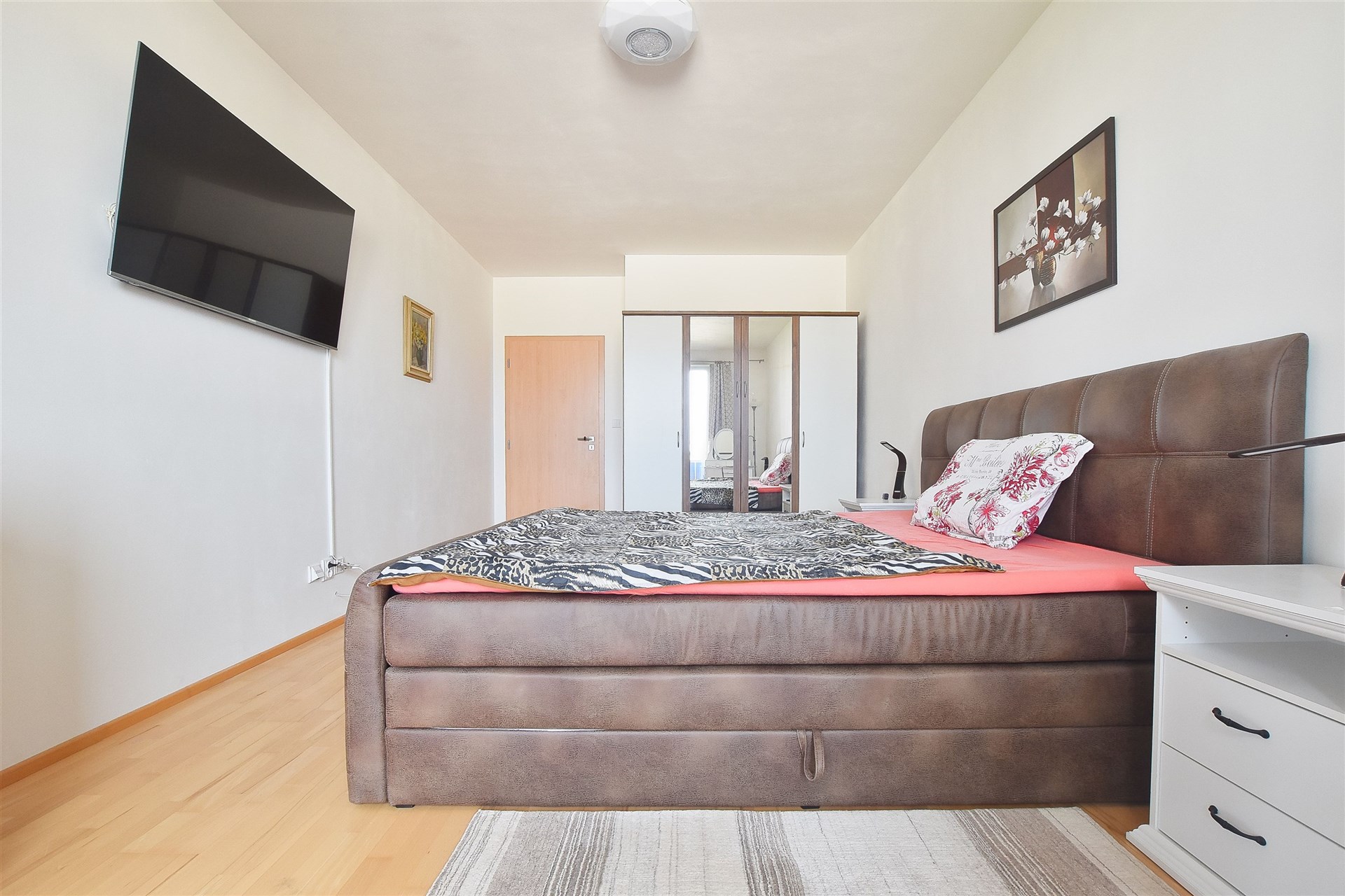Prostorná ložnice s parketovou podlahou, velkou postelí a moderním vybavením. Disponuje velkými vestavěnými skříněmi a minimalistickým stylem.