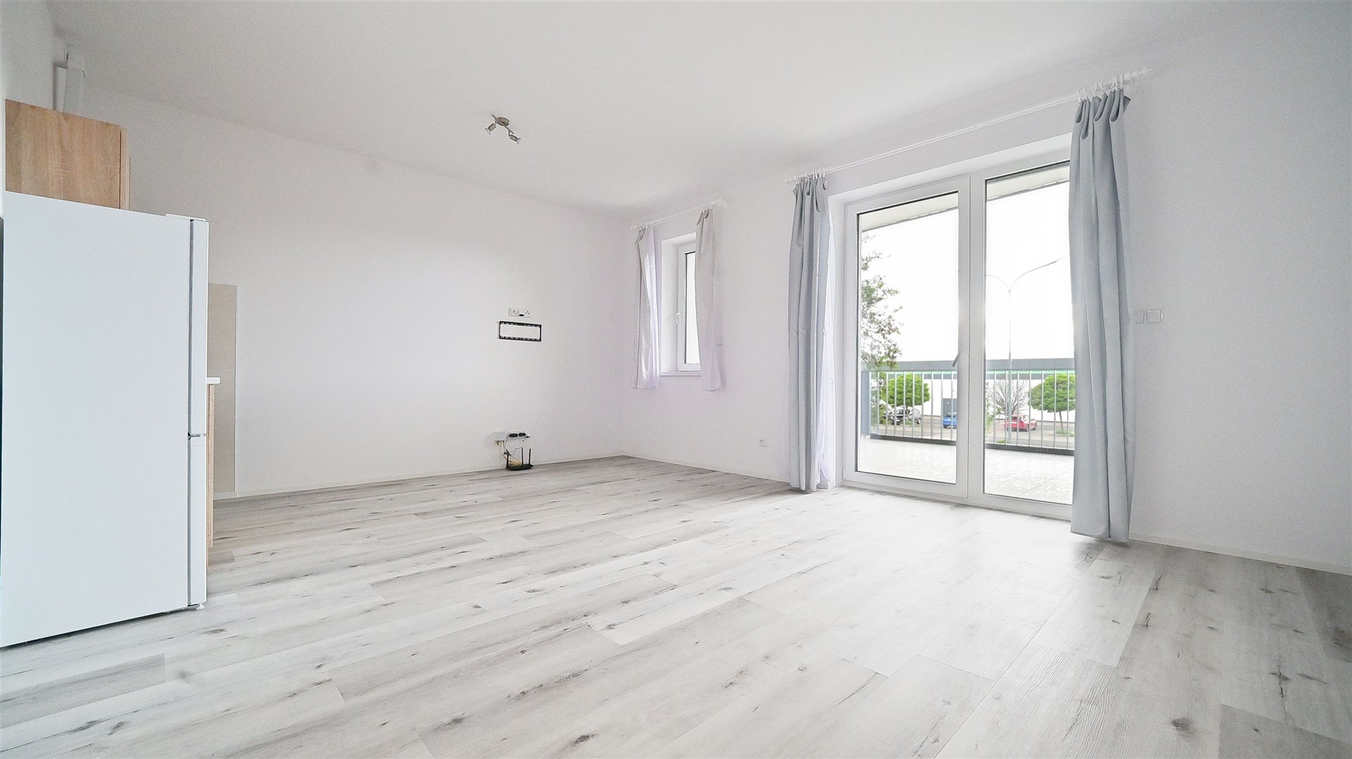 Světlý obývací pokoj s moderními francouzskými okny, světlá laminátová podlaha, rekonstruovaný prostor poskytuje příjemný výhled do okolí.