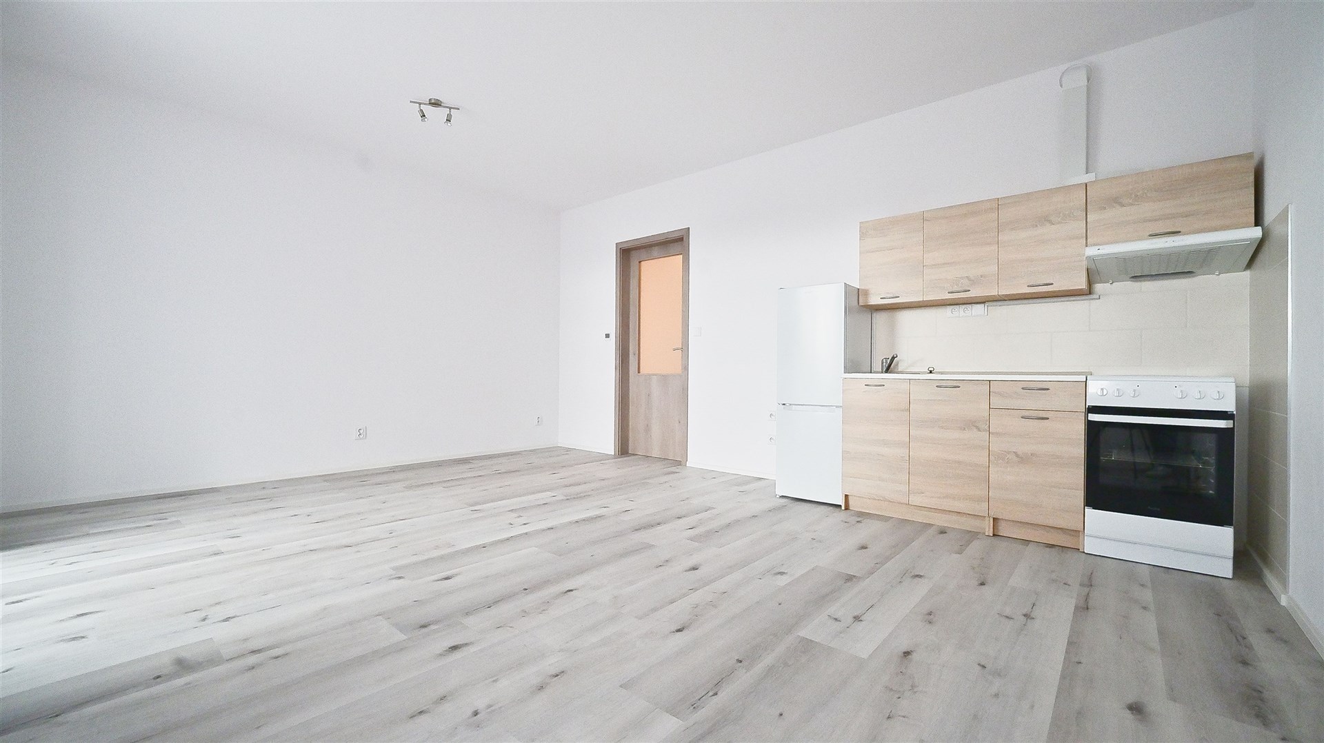 Světlý obývací pokoj s moderní kuchyní, parketová podlaha, světlé dřevěné skříňky, rekonstruovaný interiér, velká okna pro přirozené světlo.