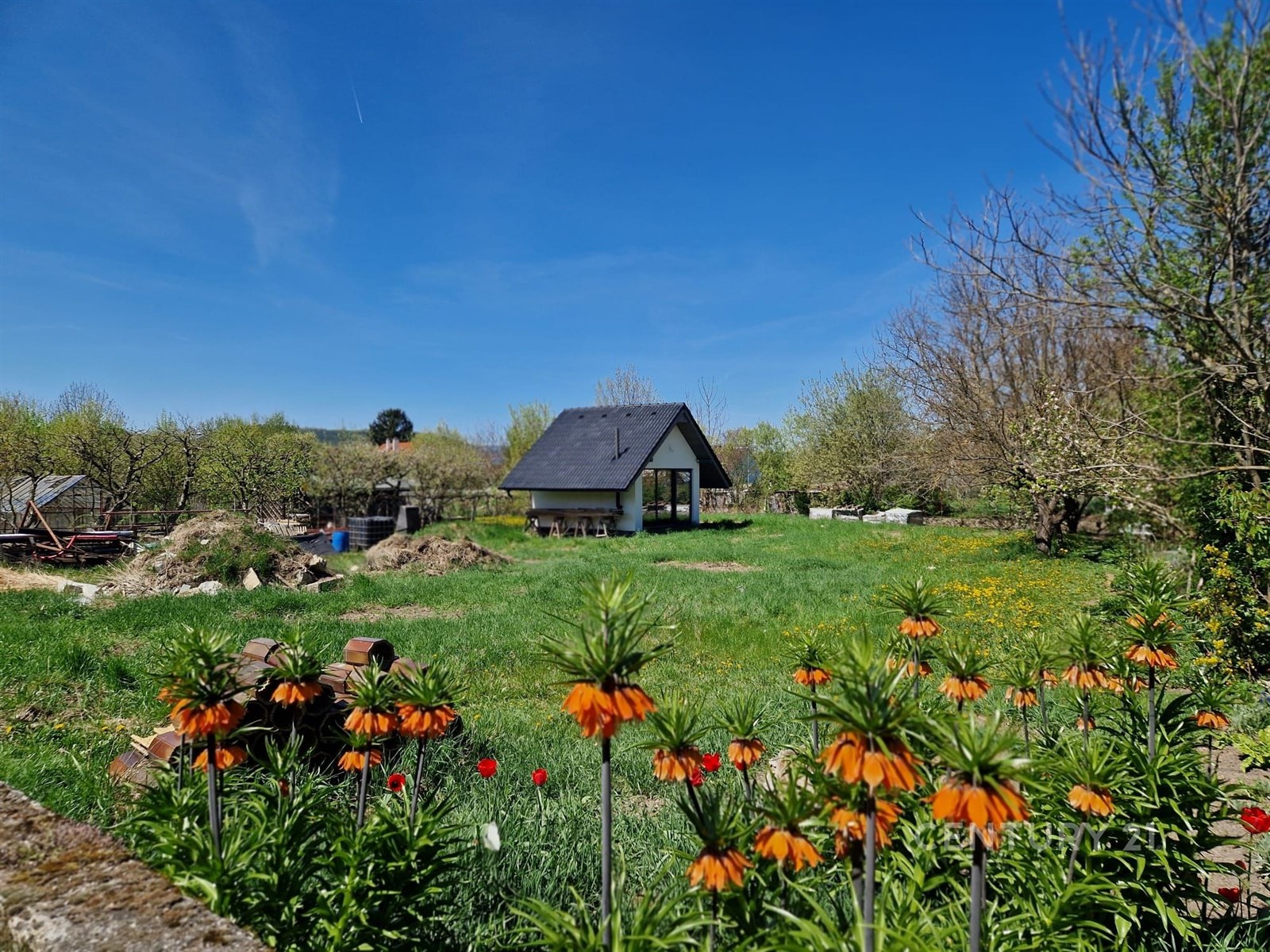 Rozlehlá zahrada s trávníkem a květinami, menší dřevěná chatka, klidná lokalita, ideální pro rekreační účely nebo zahrádkářství.