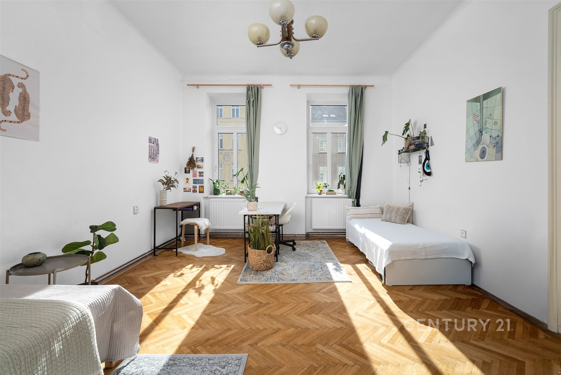 Světlý obývací pokoj s parketovou podlahou, velká okna s bílými rámy, moderní dekorace a minimalistický nábytek, ideální pro rekreační obývání.