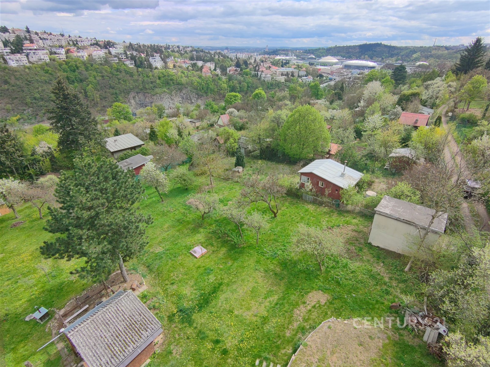 Přírodní pozemek s výhledem na krajinu, obklopen stromy a keři, v klidné lokalitě s rekreačními chatami a zelení, ideální pro milovníky přírody.