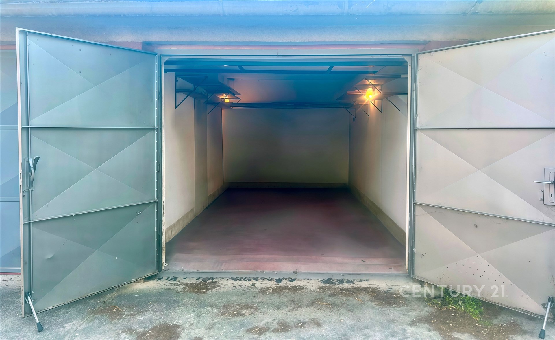 Praktická garáž s betonovou podlahou, kovovými dveřmi a elektrickým osvětlením, vhodná pro bezpečné parkování a uložení vozidla.