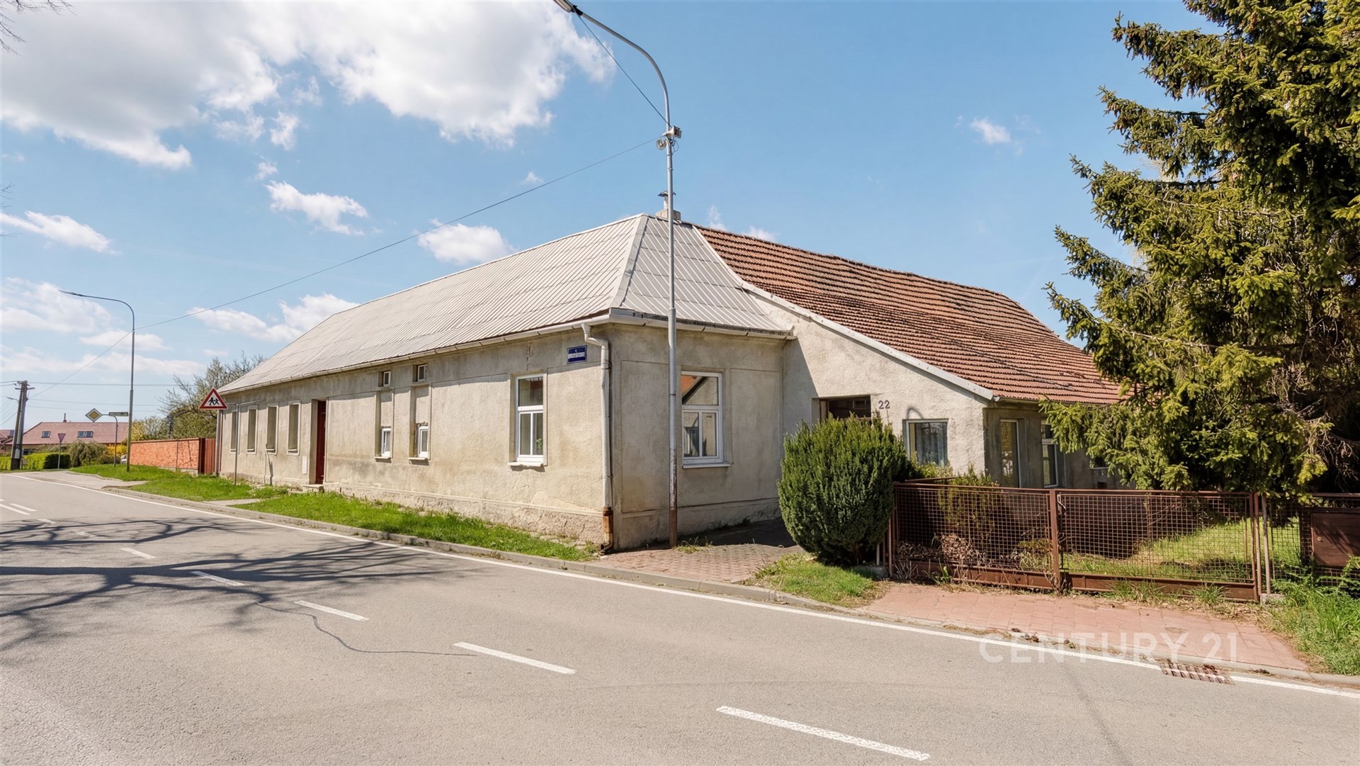Tradiční vesnický dům s šikmou střechou a velkou zahradou, umístěný u hlavní silnice, vhodný k částečné rekonstrukci nebo úpravám.