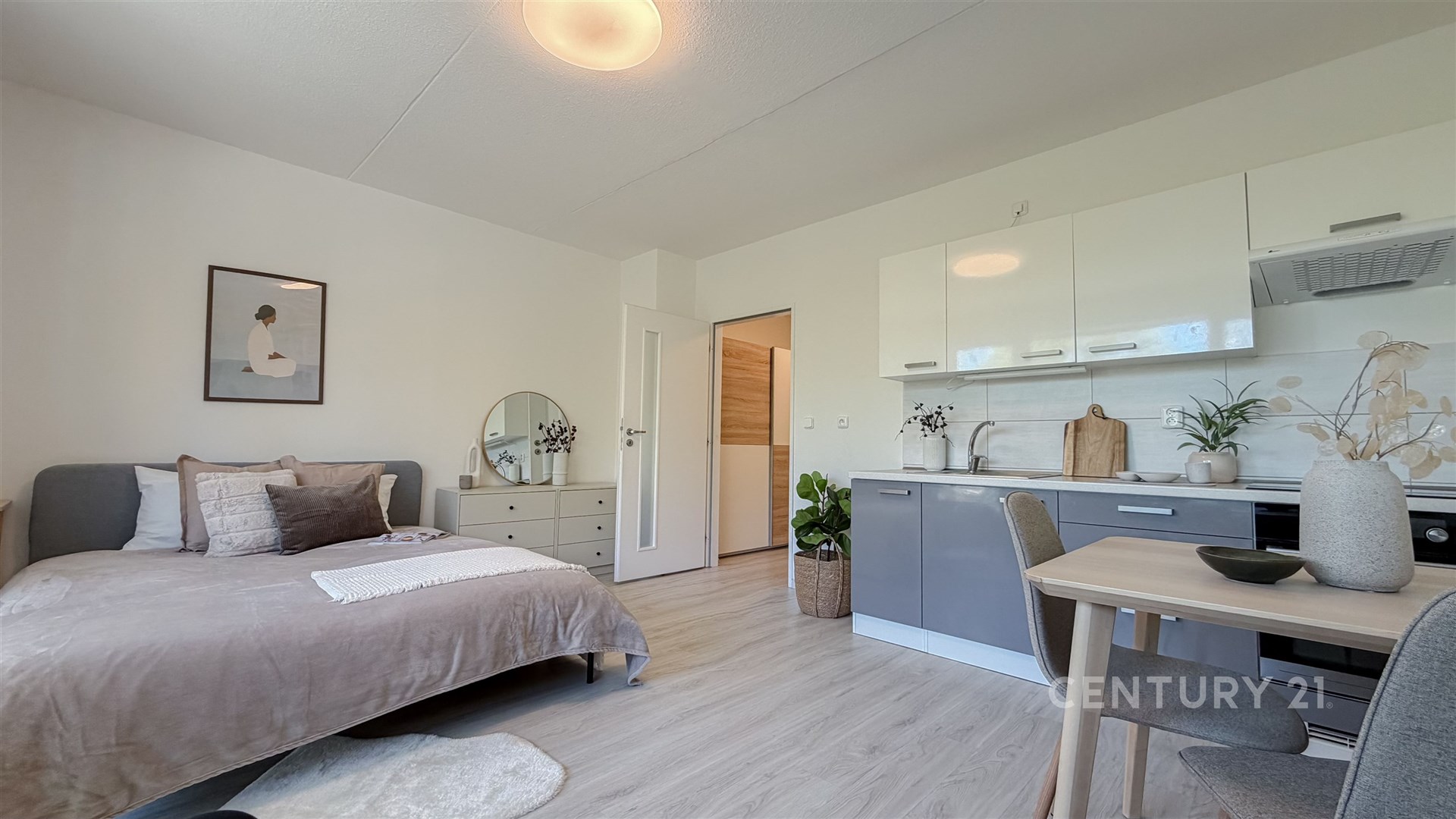 Kompaktní studio s moderní kuchyní, světlá plovoucí podlaha, elegantní nábytek, dostatek denního světla, minimalistický design.