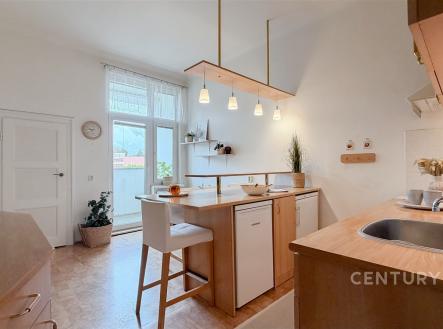Světlá kuchyň s moderními spotřebiči, parketovou podlahou a velkými okny, které poskytují dostatek přirozeného světla.