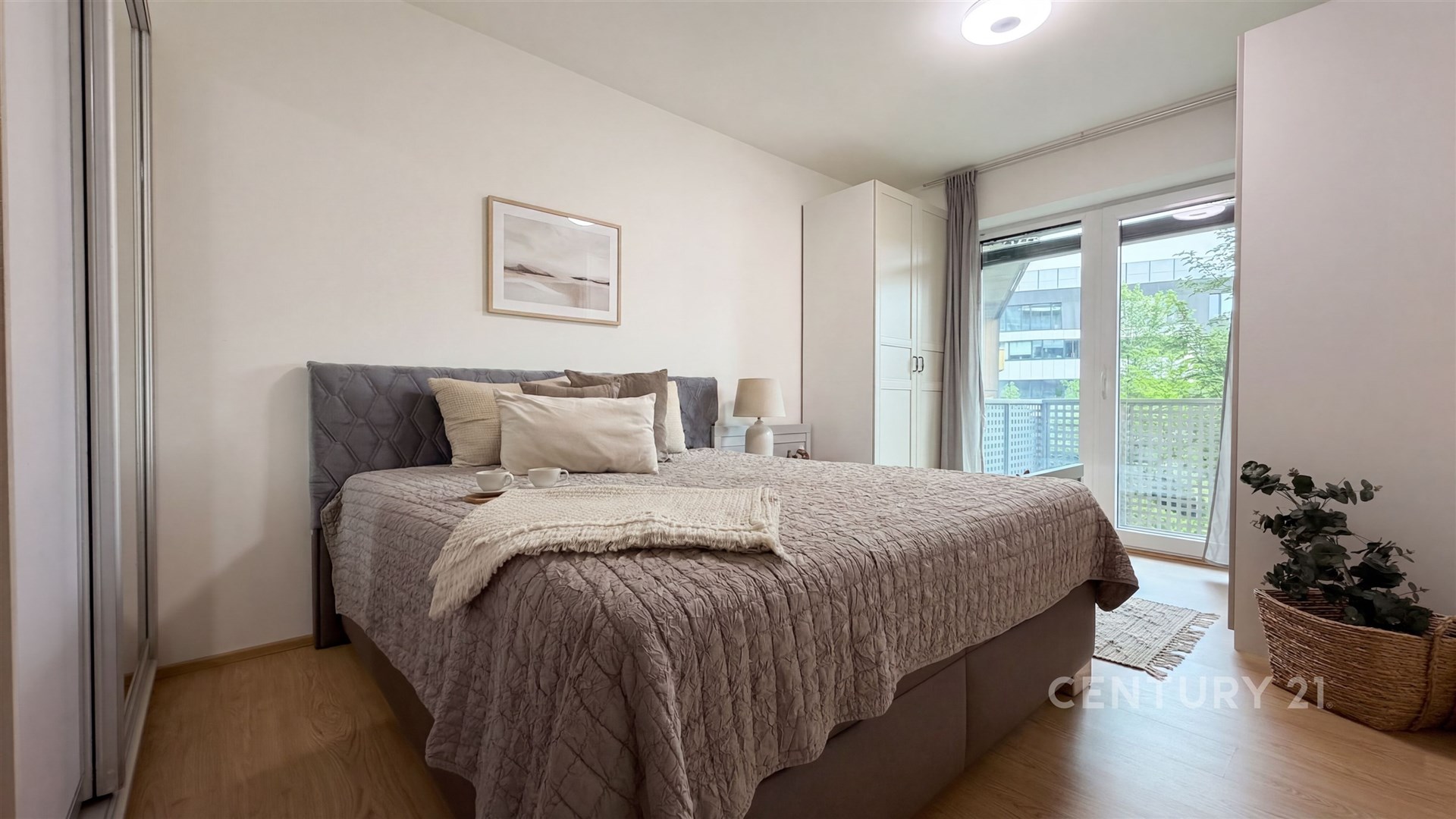 Světlá ložnice s moderním stylem, parketová podlaha, velká okna vedoucí na balkon, vestavěné skříně poskytující dostatek úložného prostoru.