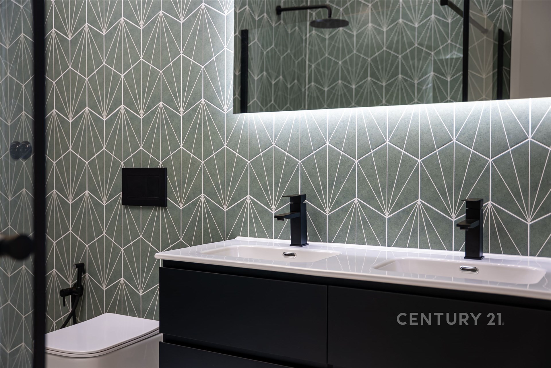 Moderní koupelna s tmavou dlažbou, designové obklady a velké zrcadlo. Elegantní umyvadlo s integrovaným osvětlením a černé doplňky.