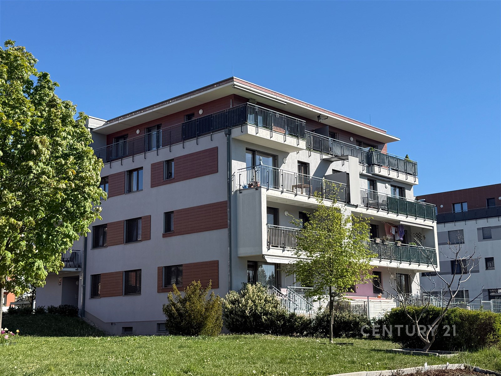 Exteriér moderního bytového domu s rozsáhlými balkony, parkovou zelení a světlou fasádou v klidné čtvrti.