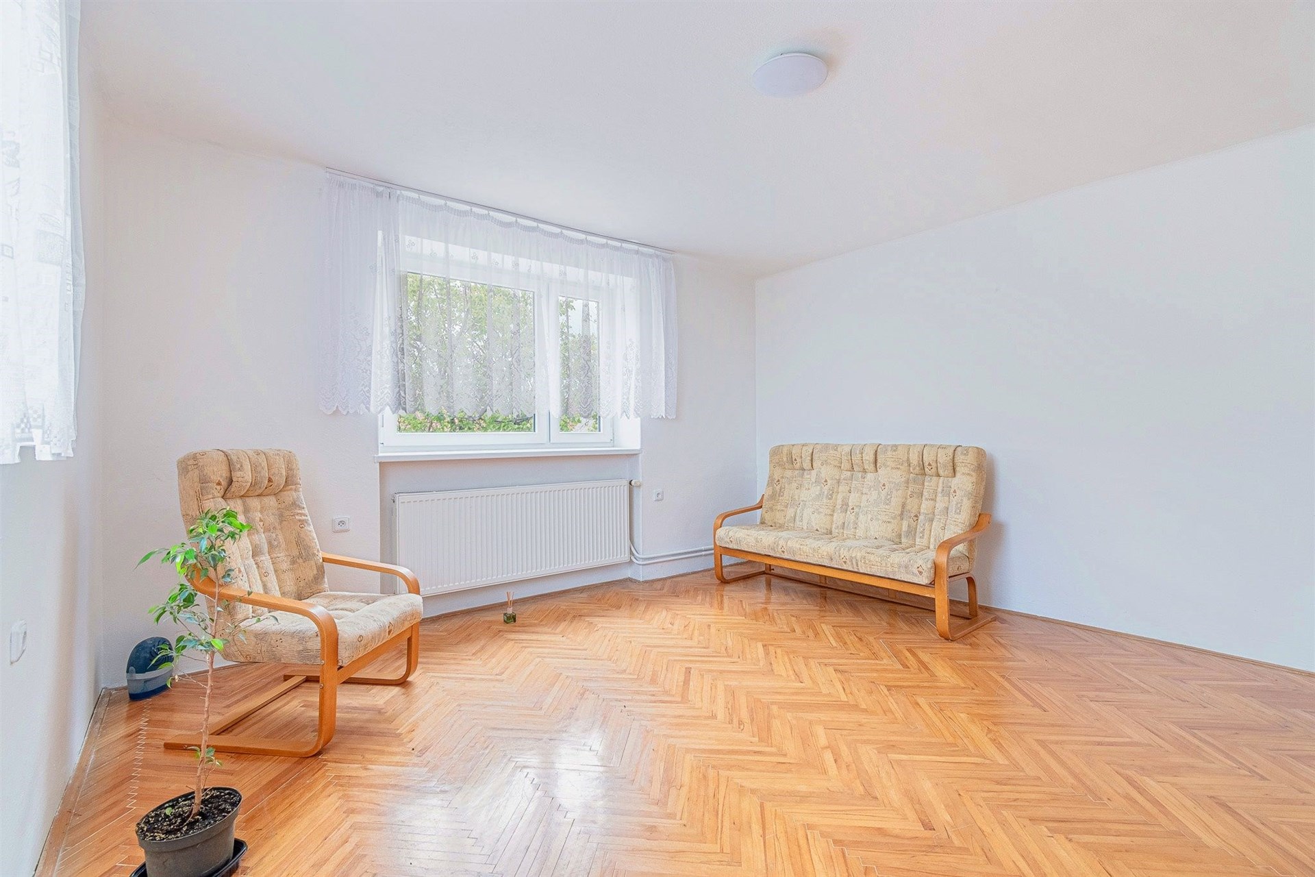 Světlý obývací pokoj s parketovou podlahou a velkými okny, moderní interiér, neutrální barevné schéma poskytuje útulnou atmosféru.