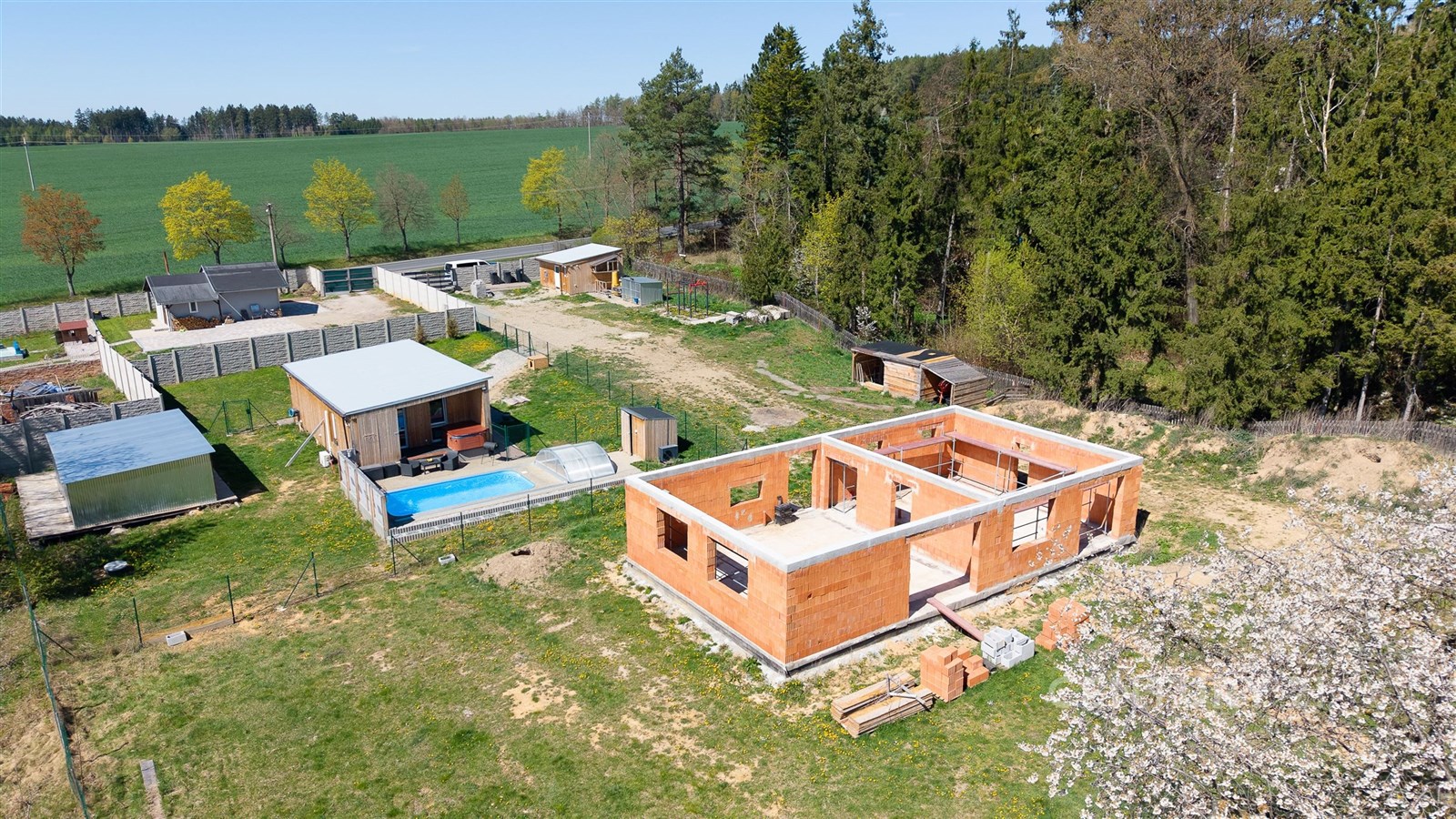 Stavební pozemek se zahájenou konstrukcí domu, obklopený zelení, cihlová stavba, klidná lokalita, možnost dokončení výstavby podle vlastních představ