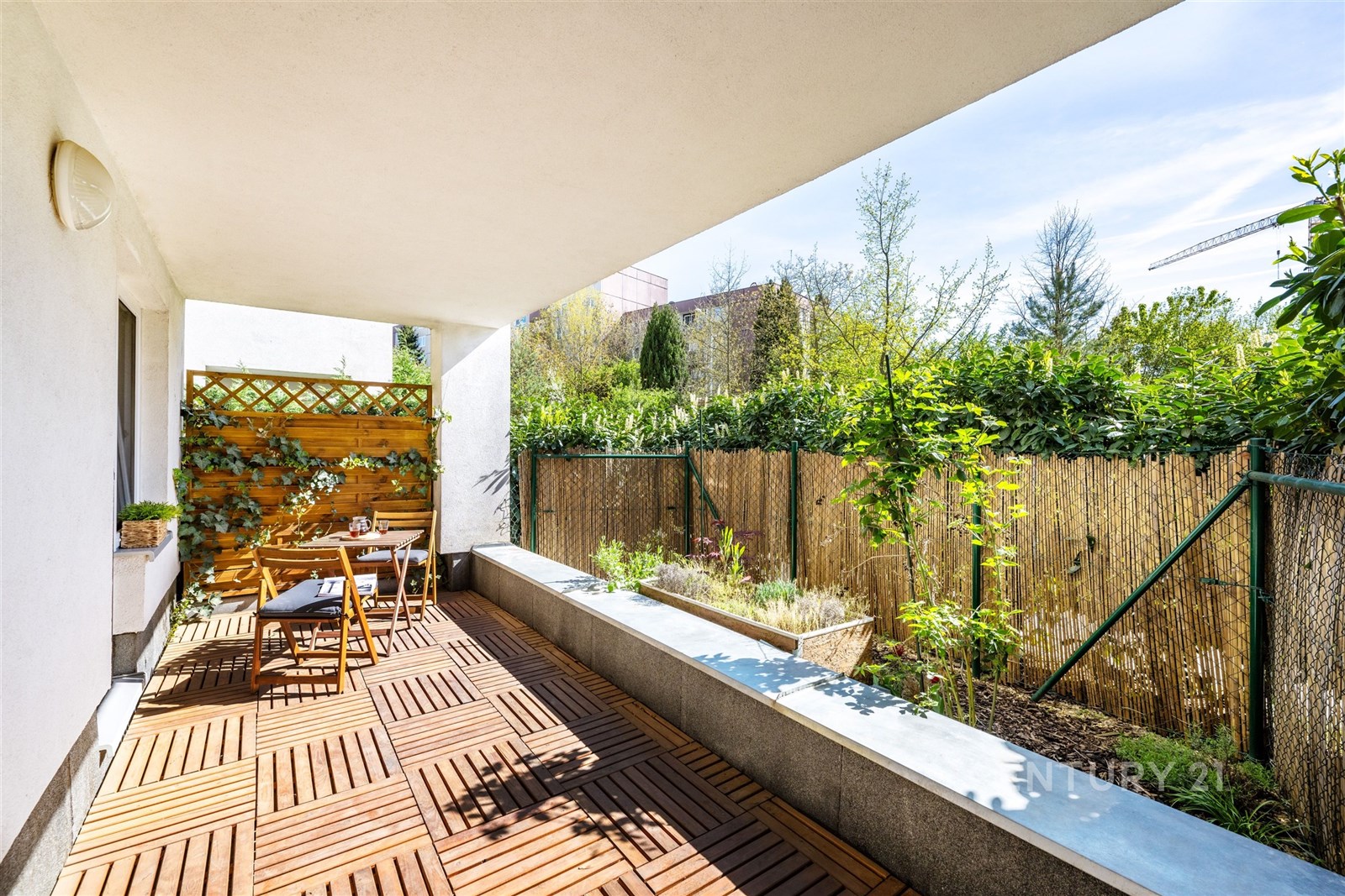 Prostorná terasa s dřevěnou podlahou nabízí relaxační zónu s venkovním posezením, ohraničenou zelení a vysokým plotem pro soukromí.