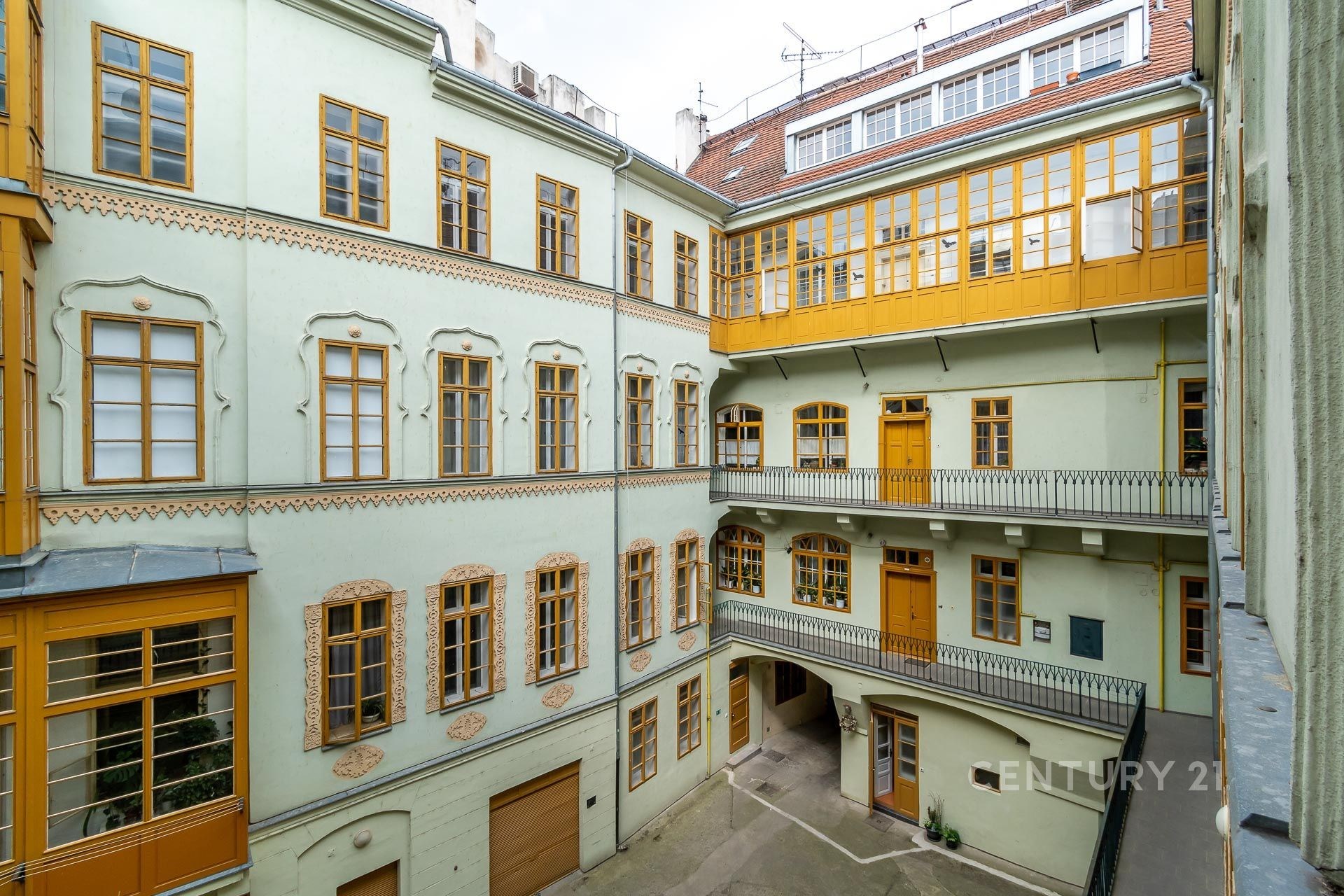 Historická fasáda se zdobenými okny a velký dvůr. Budova má světlé omítky a zachovalé dřevěné prvky, které dodávají kouzlo.