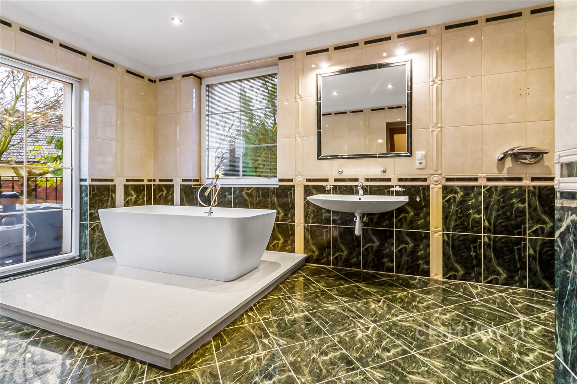 Luxusní koupelna s mramorovou dlažbou, volně stojící vanou a velkými okny. Moderní design a kvalitní materiály poskytují elegantní prostor.