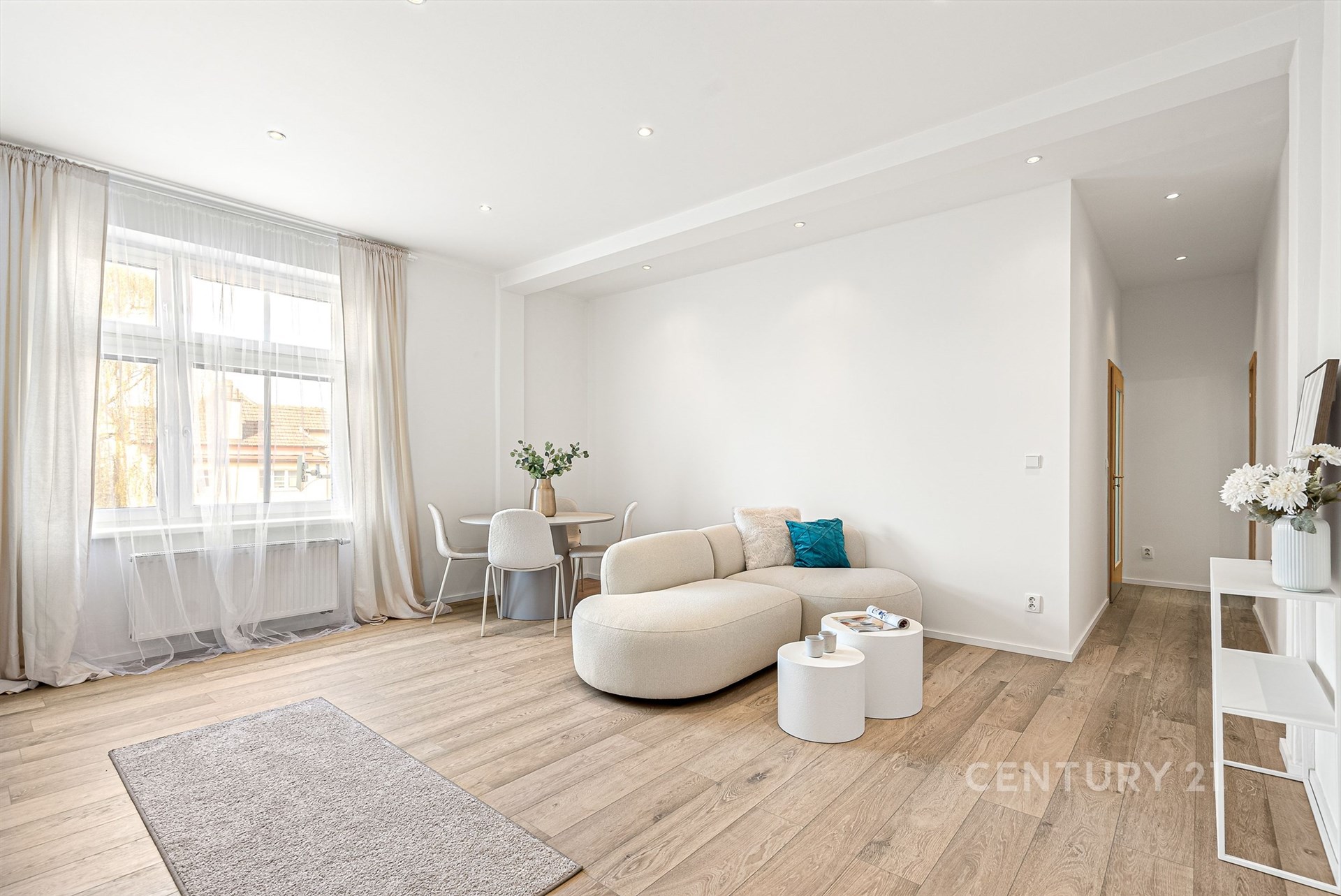 Světlý obývací pokoj s moderním designem, parketová podlaha a velká okna, které zajišťují dostatek přirozeného světla, nabízí komfortní bydlení.