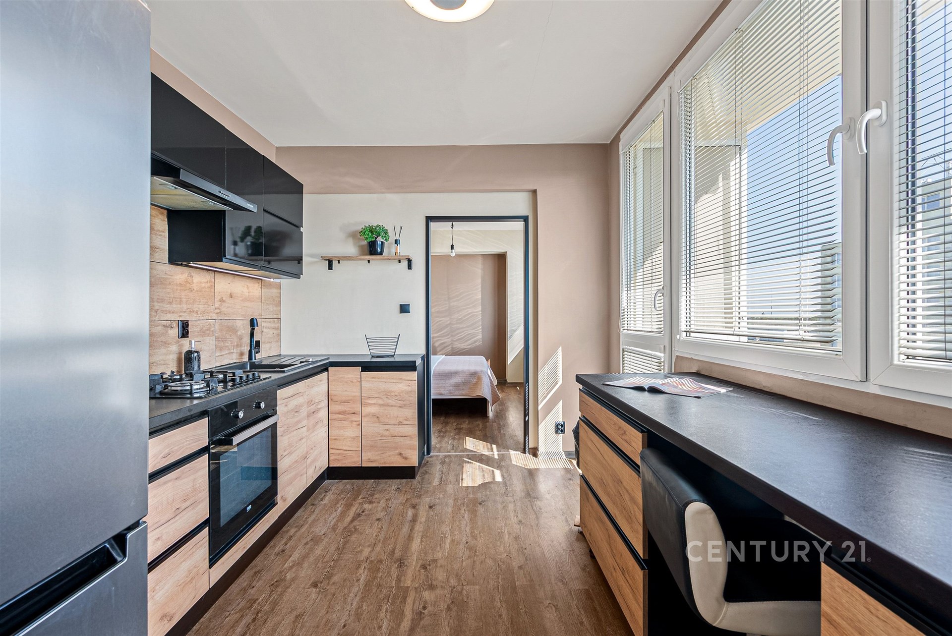 Moderní kuchyň s dřevěnými prvky a vestavěnými spotřebiči, světlá díky velkým oknům. Parketová podlaha a elegantní design přináší útulnost.