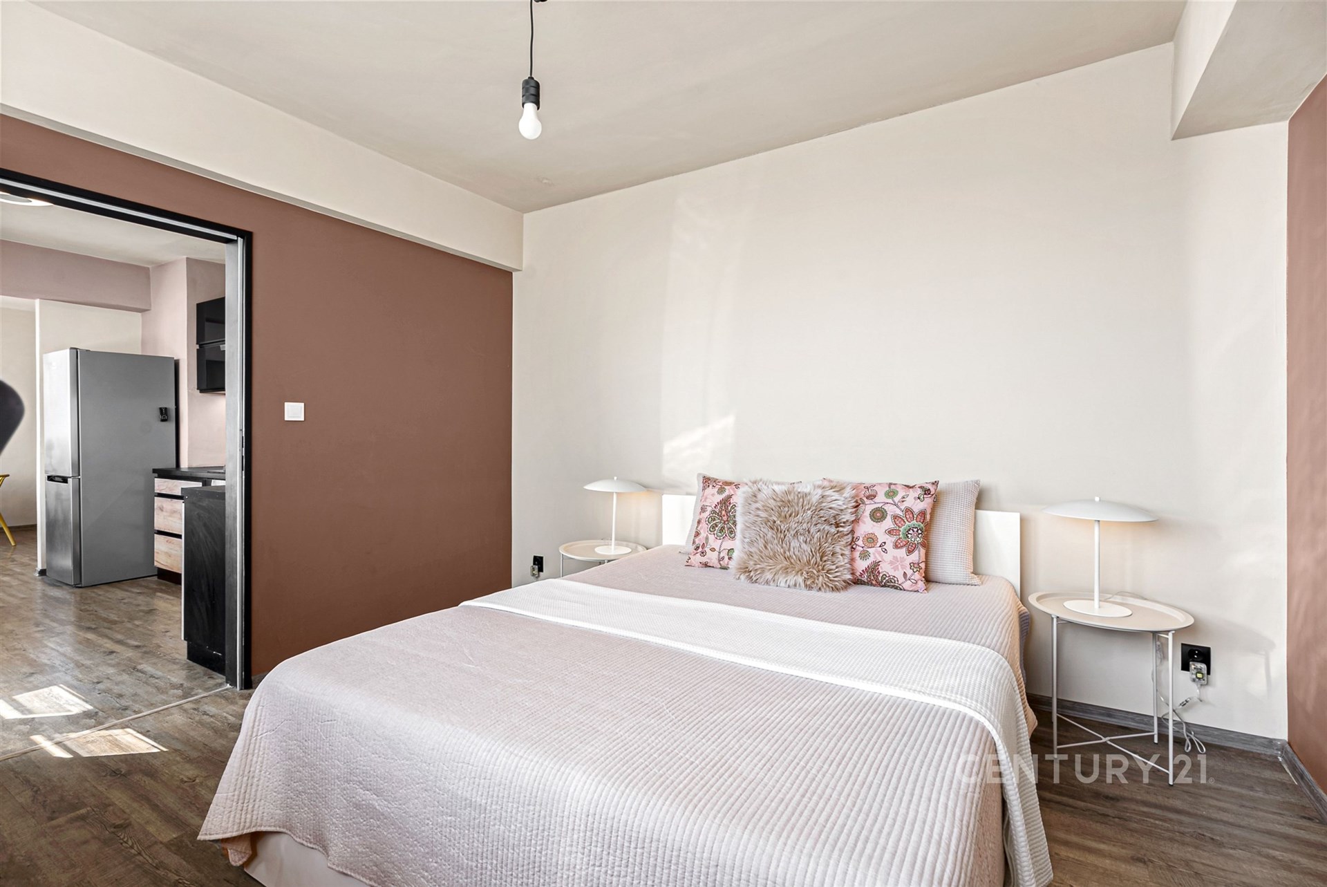 Prostorná ložnice s dřevěnou podlahou, moderními lampami a světlými stěnami, doplněná velkou postelí se stylovými polštáři.