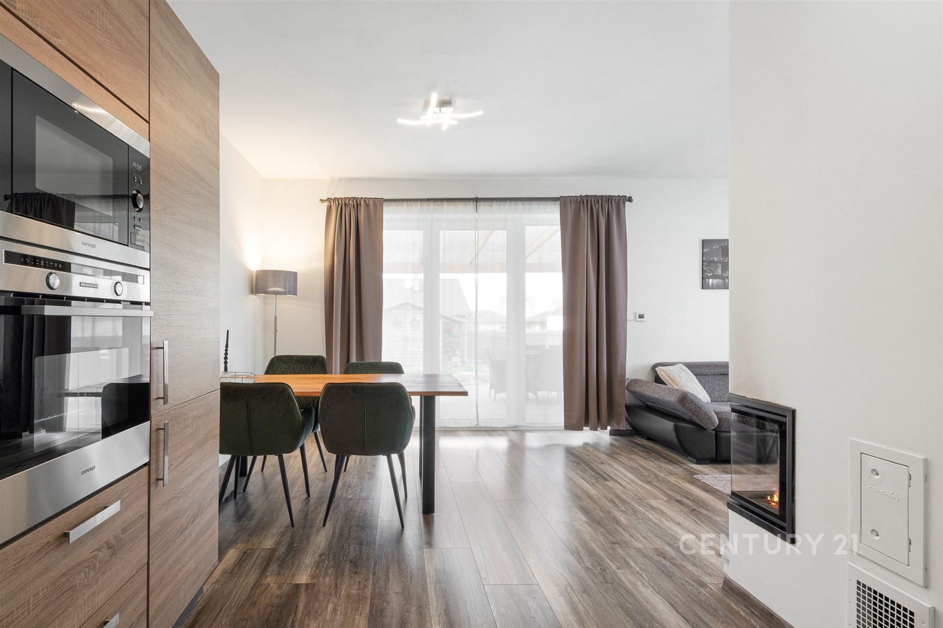 Moderní obývací pokoj s kuchyní, parketová podlaha, velká okna, světlý interiér s vestavěnými spotřebiči a elegantním nábytkem.