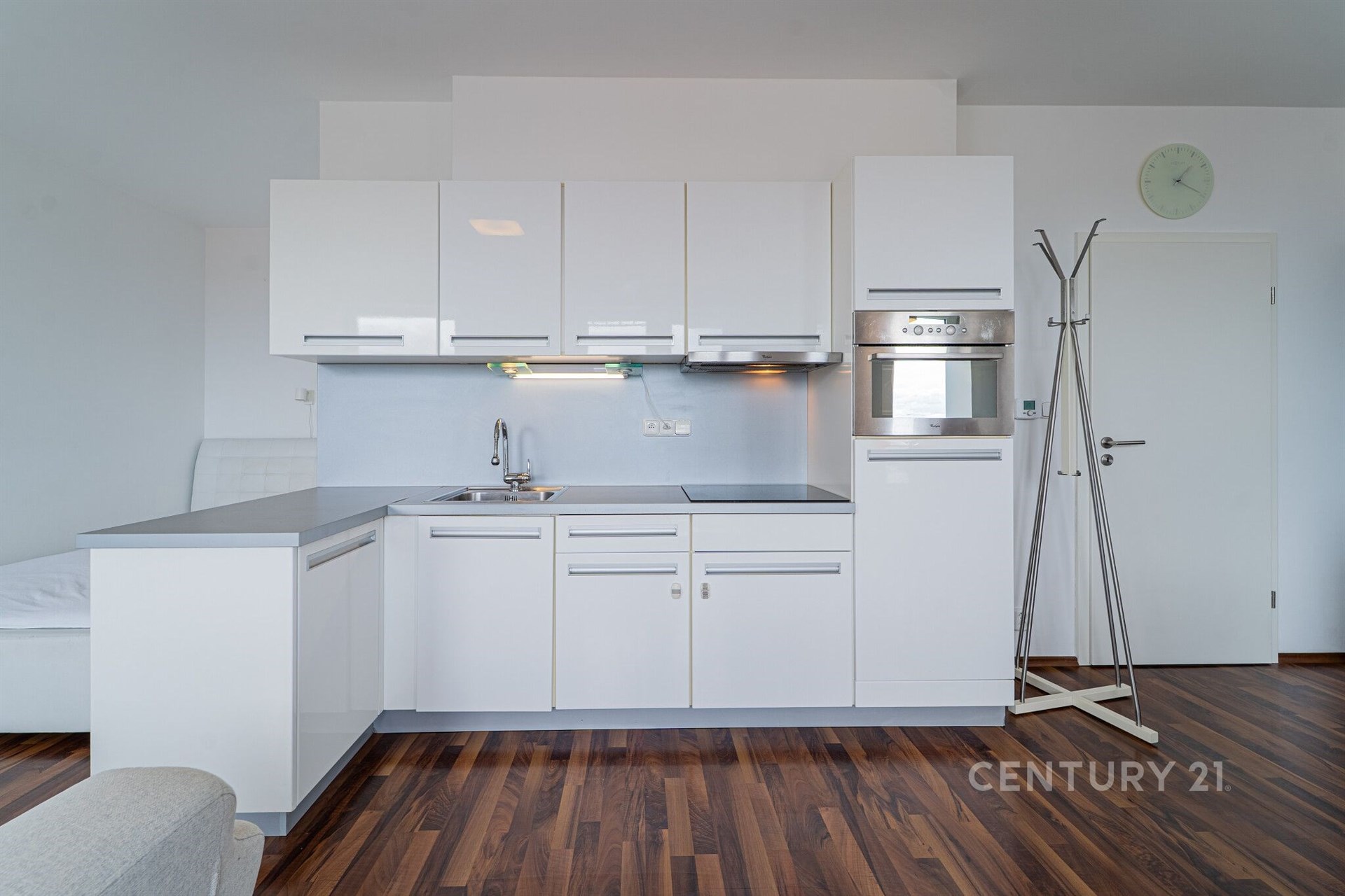 Moderní kuchyň s bílými lesklými skříňkami, vestavěnou troubou a parketovou podlahou, prostorný design pro pohodlné bydlení.