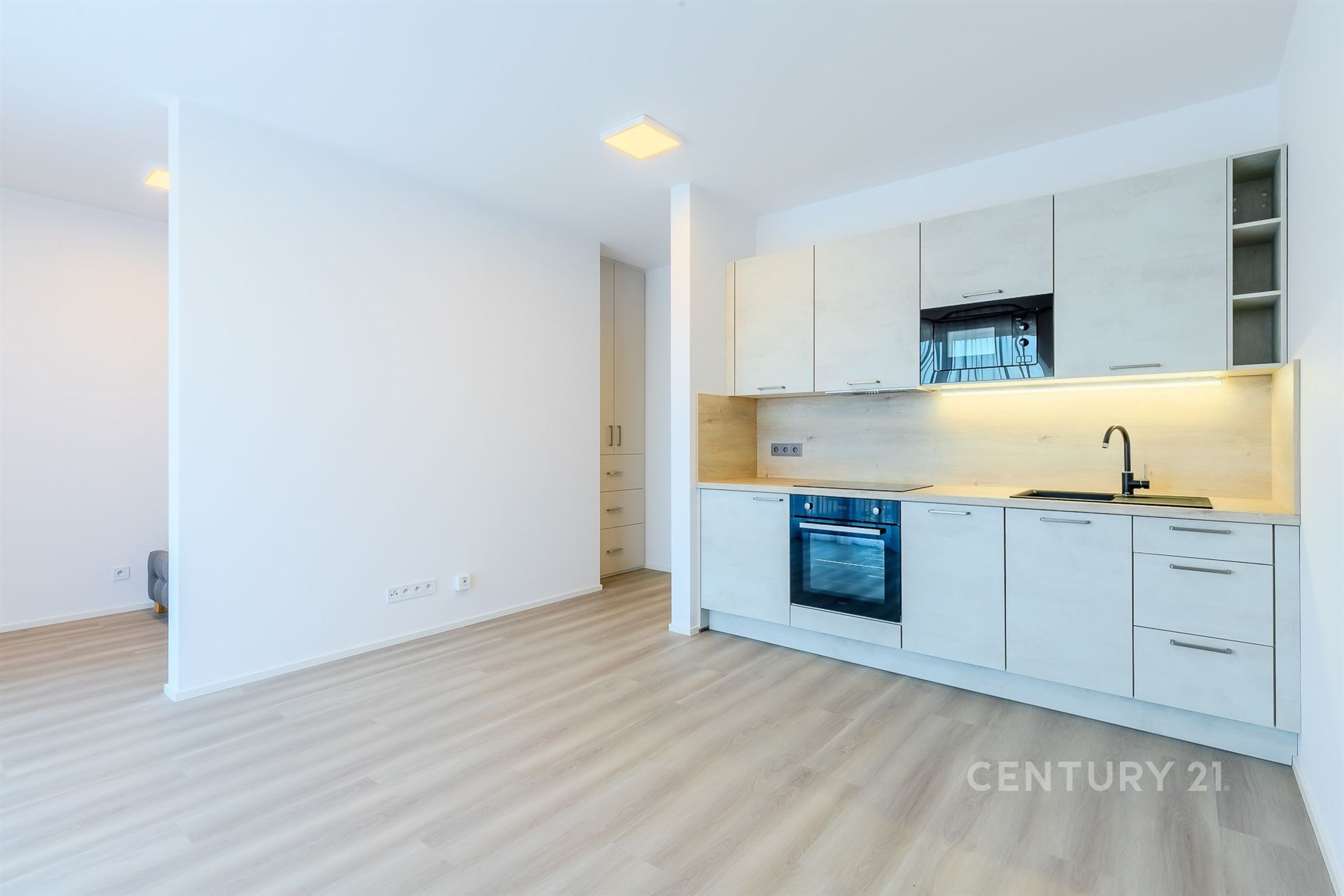 Moderní kuchyň s parketovou podlahou, světlým minimalistickým designem, vestavěnými skříněmi a moderními spotřebiči.