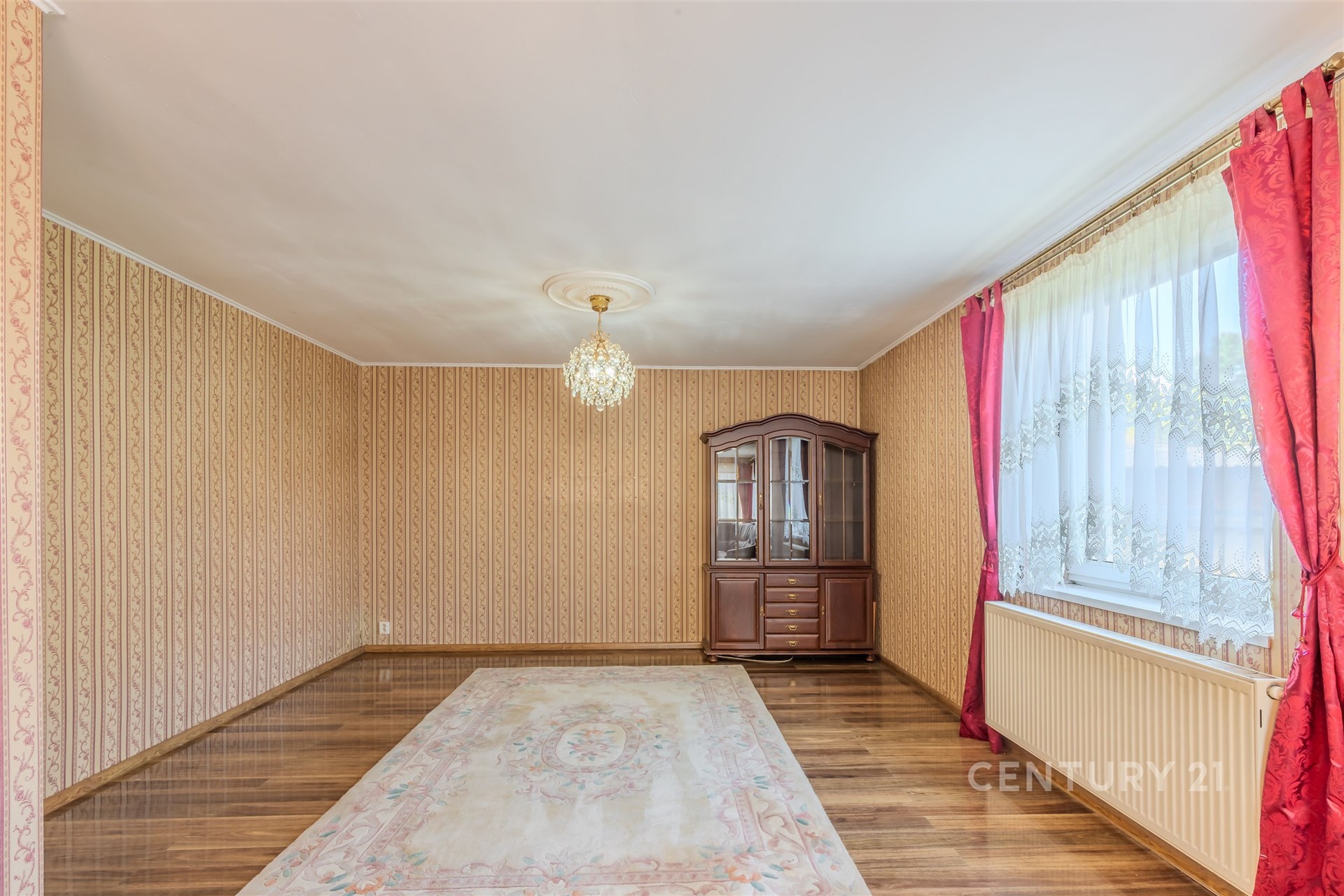 Tradiční obývací pokoj s parketovou podlahou, velkým oknem a elegantními závěsy, klasický styl a dřevěný nábytek dotvářejí útulnou atmosféru