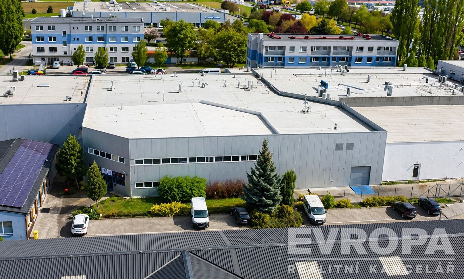 Průmyslová hala s moderní fasádou, rovnou střechou a parkovacími místy, ideální pro výrobu či skladování.