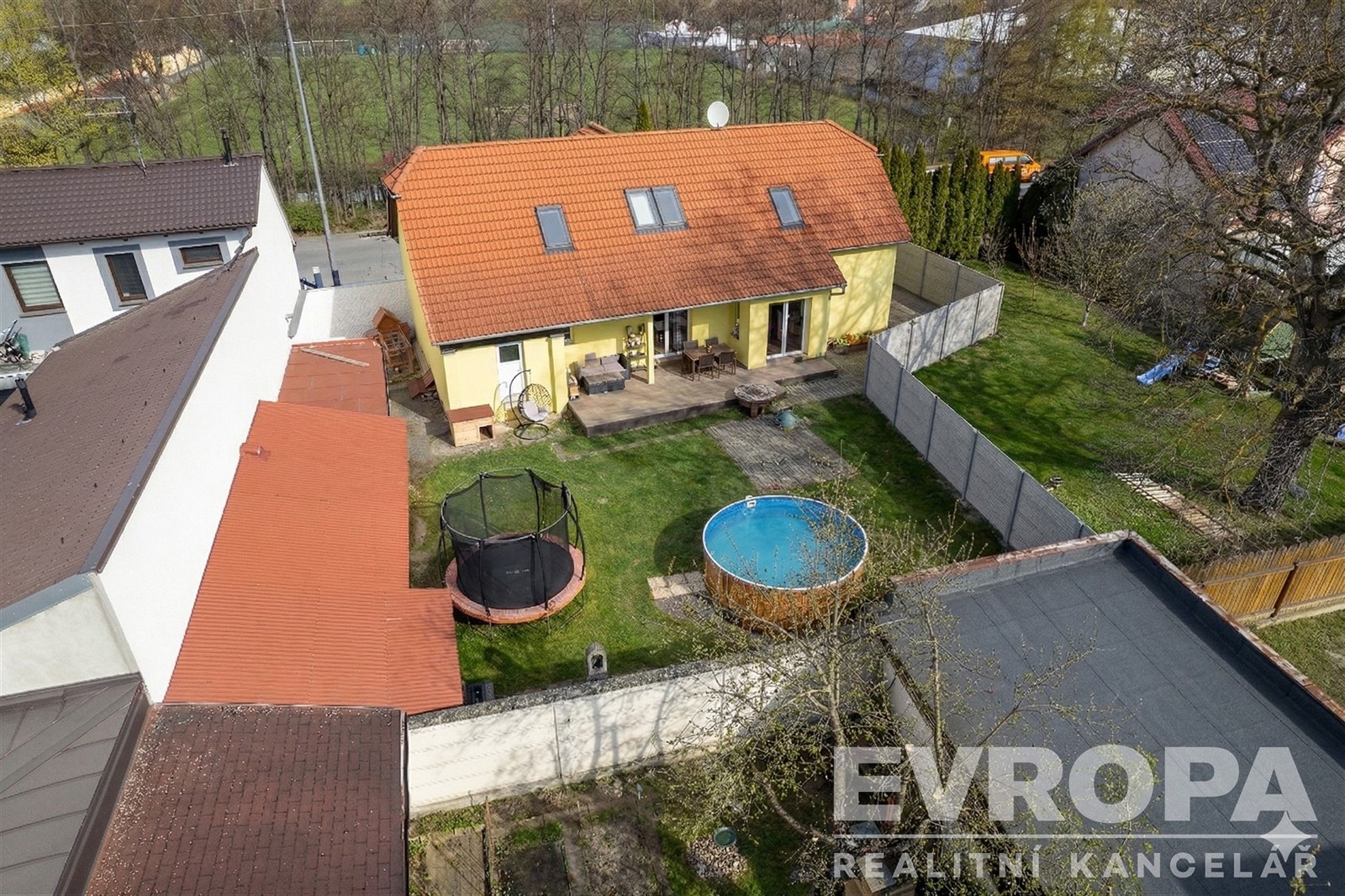 Zahrada s rodinným domem, terasou a bazénem. Zahrada nabízí trávník, dřevěné doplňky a trampolínu, ideální pro relaxaci a rodinný život.