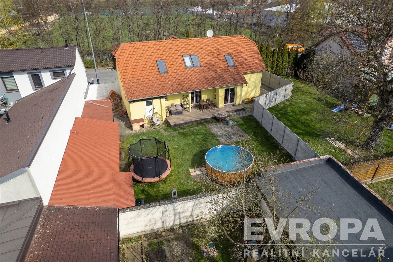 Rodinný dům se zahradou, moderní žlutá fasáda, červená střecha, prostorný dvůr s trampolínou a bazénem, klidná rezidenční lokalita.