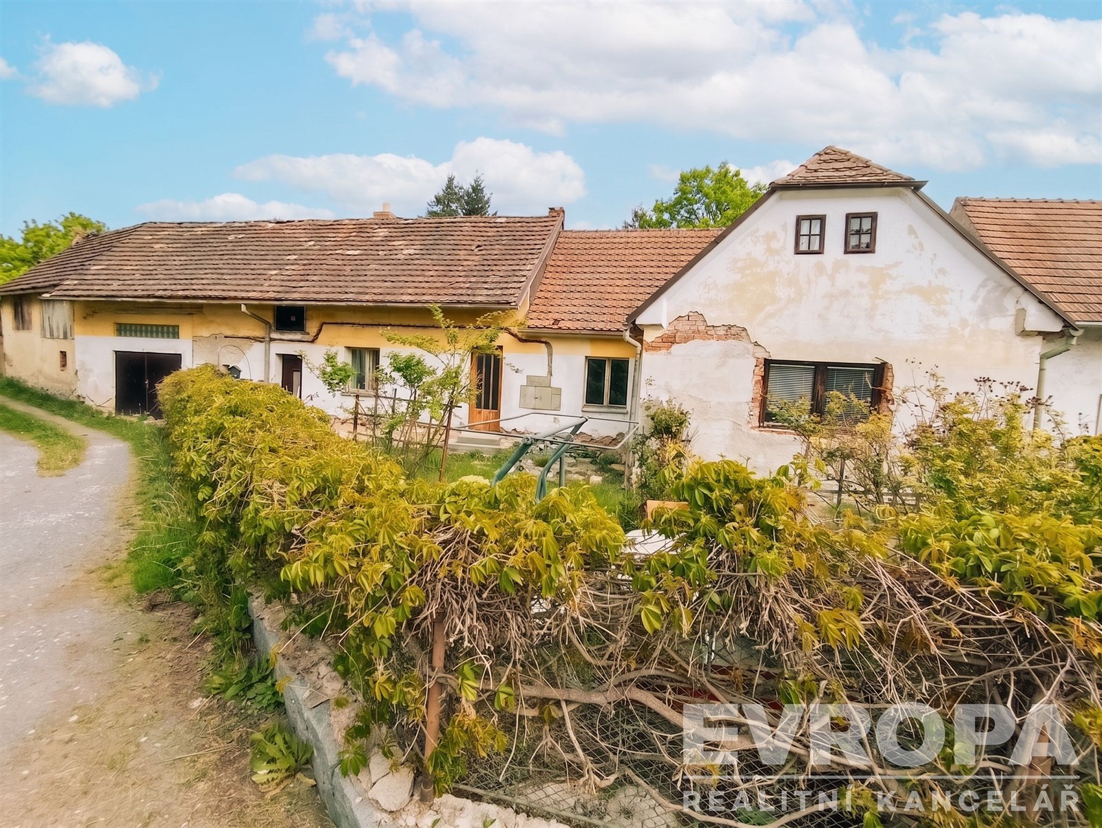 Starý rodinný dům s venkovskou atmosférou, částečně omítnutá fasáda, dřevěná okna, zahrada obklopená kamennou zdí, klidná lokalita.