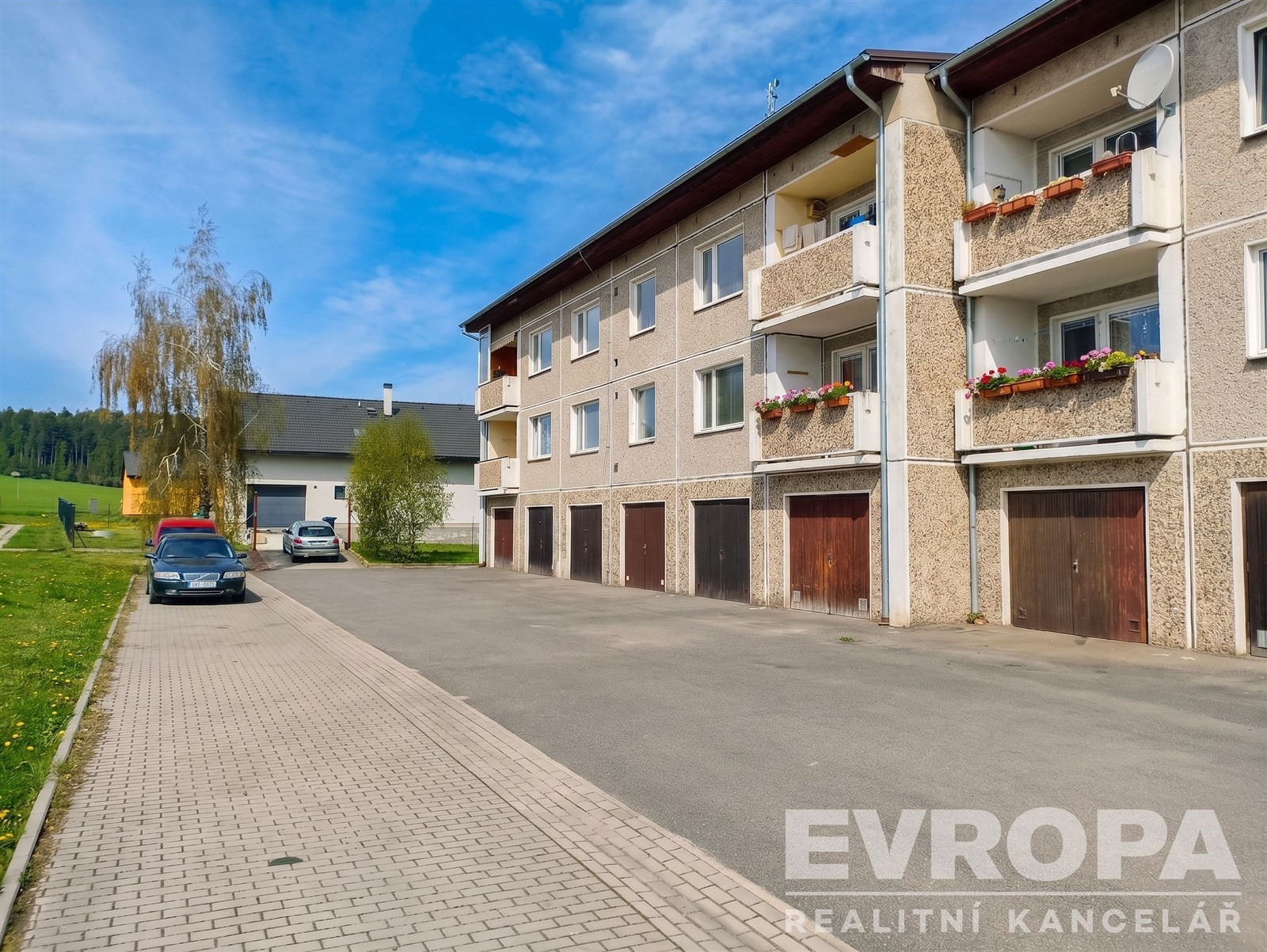 Bytový dům s garážemi, zděná konstrukce a balkony. Klidná lokalita, dobře udržovaná fasáda, prostorné parkování před budovou.