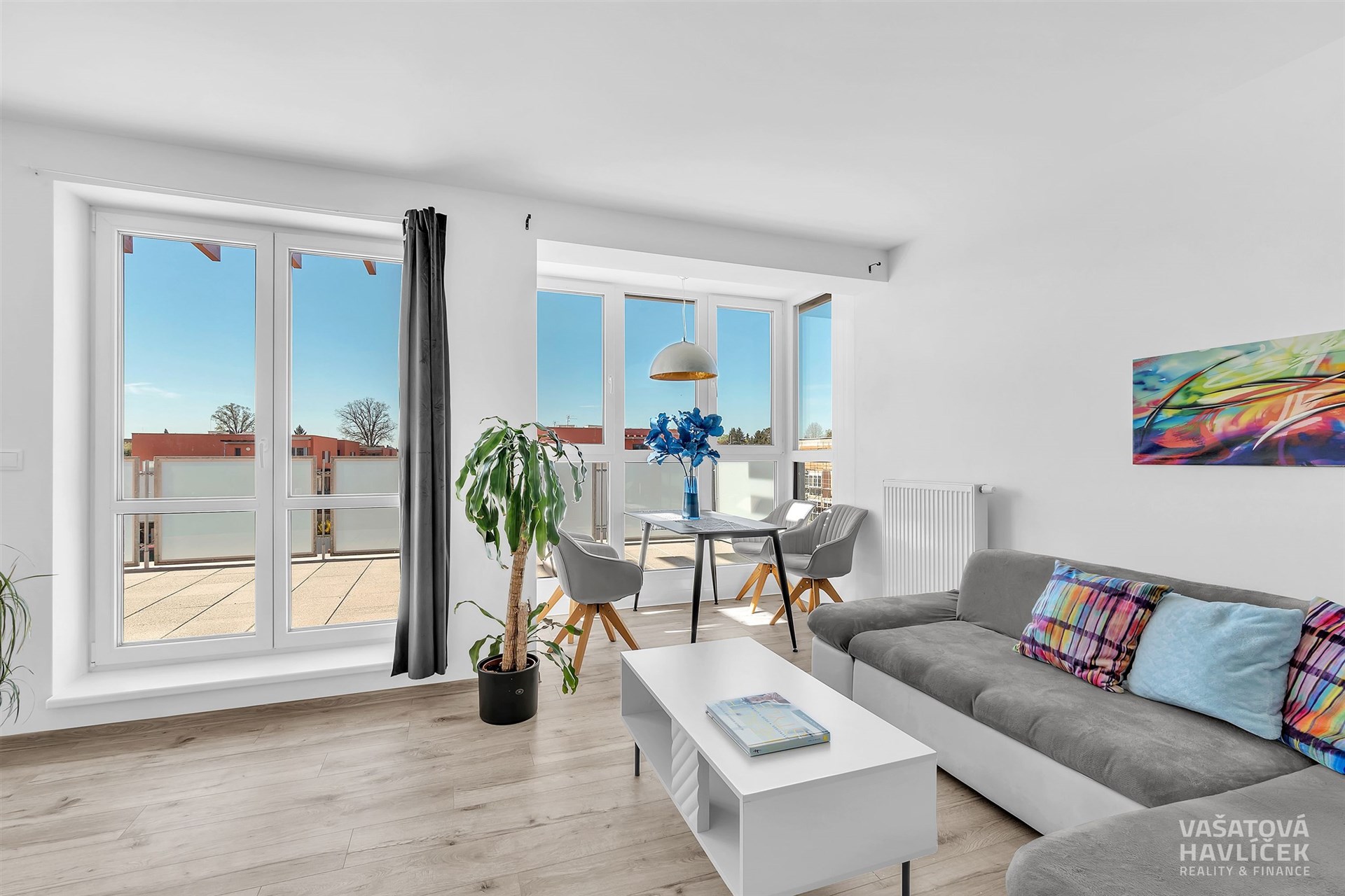 Světlý obývací pokoj s moderní parketovou podlahou, velkými okny a elegantním nábytkem, poskytuje přístup na prostorný balkon