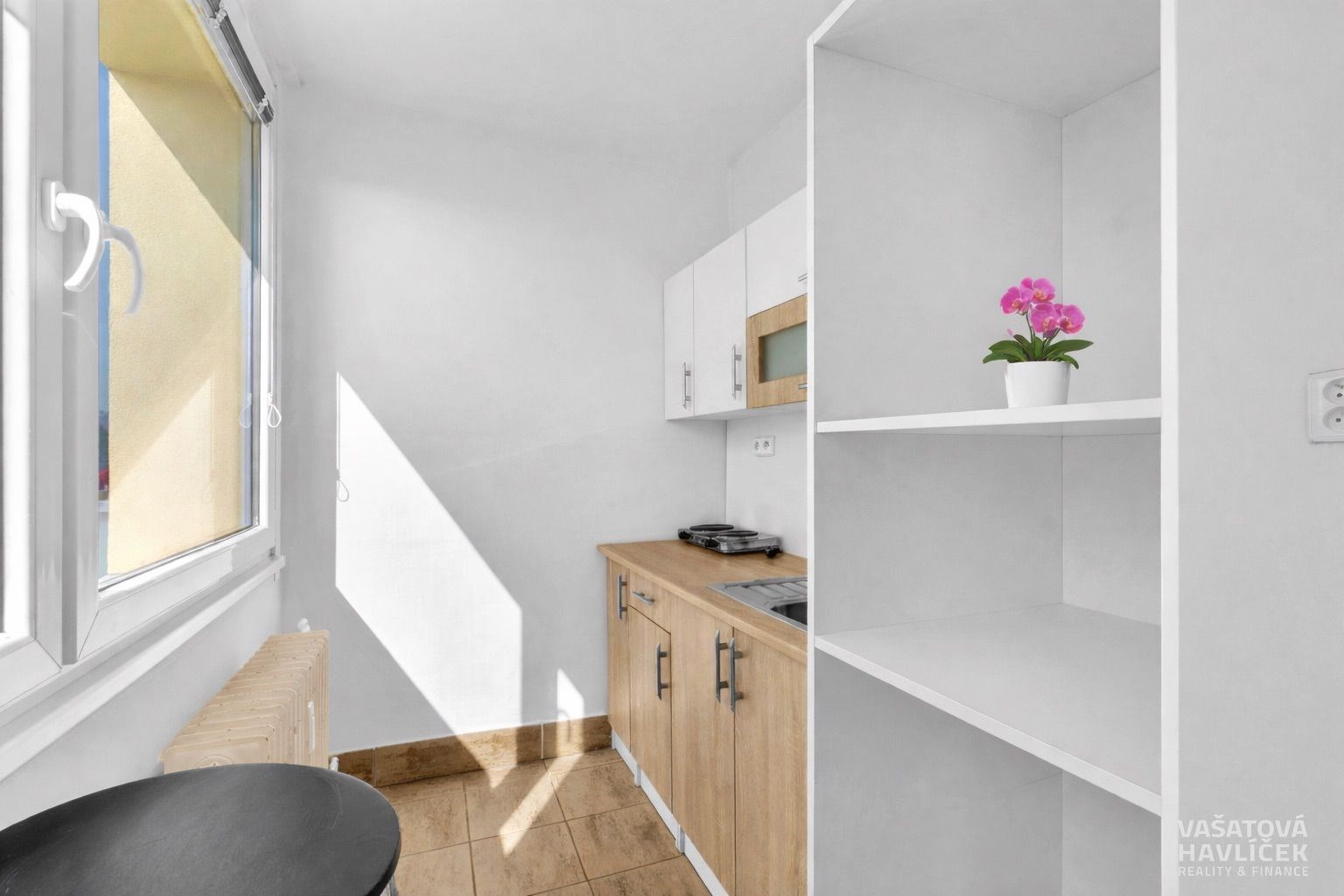 Kompaktní kuchyň s dřevěnou pracovní deskou, vestavěným úložným prostorem a velkými okny, která poskytují přirozené světlo.