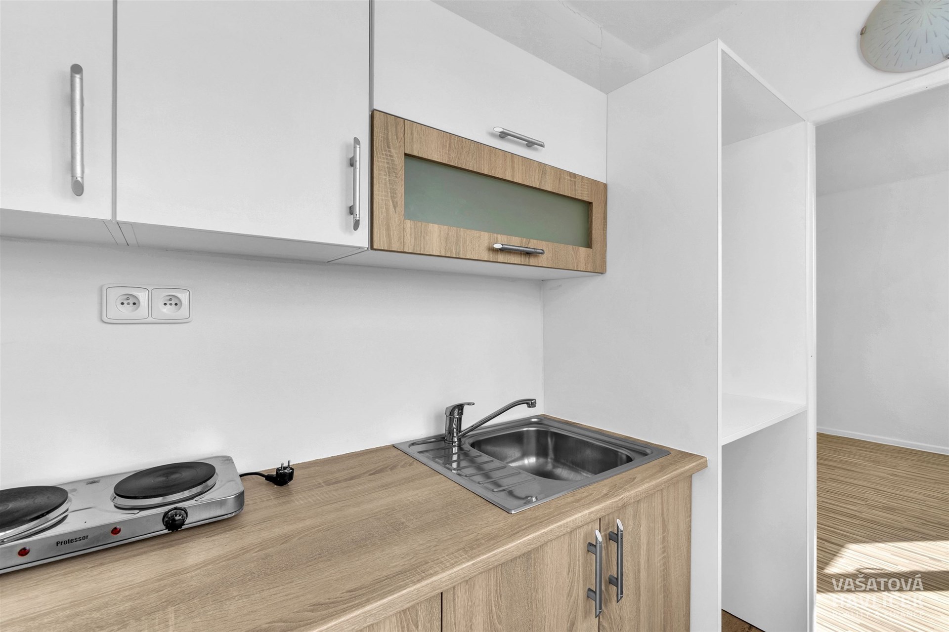 Moderní kuchyň s dřevěnou pracovní deskou a nerez dřezem, bílými skříňkami a elektrickou varnou deskou, světlý minimalistický design.