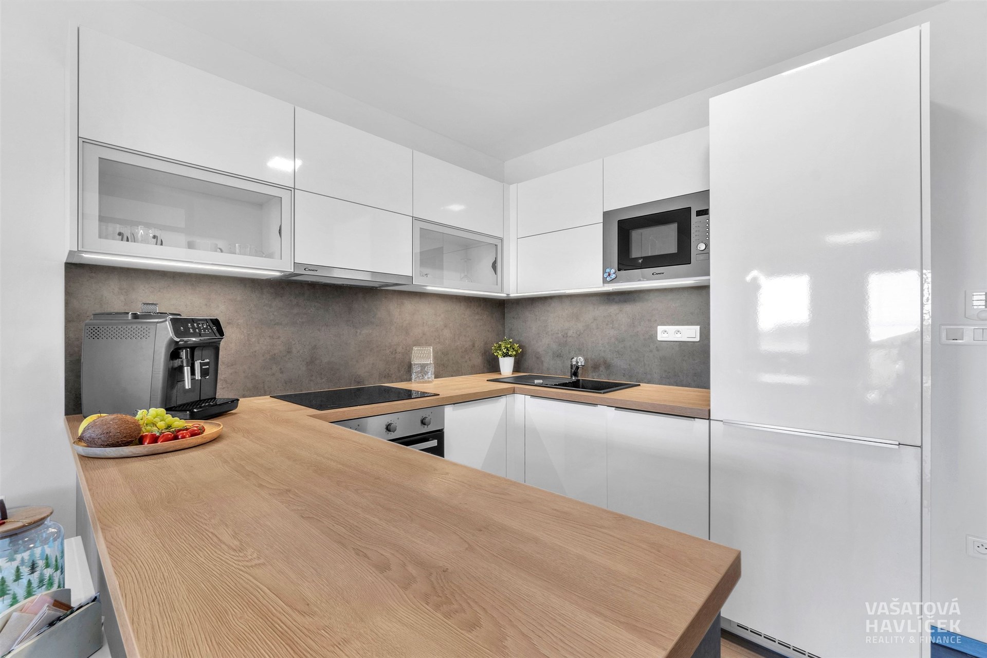 Moderní kuchyň s dřevěnou pracovní deskou, bílými skříněmi a vestavěnými spotřebiči. Světlý prostor s elegantním designem a praktickým uspořádáním.