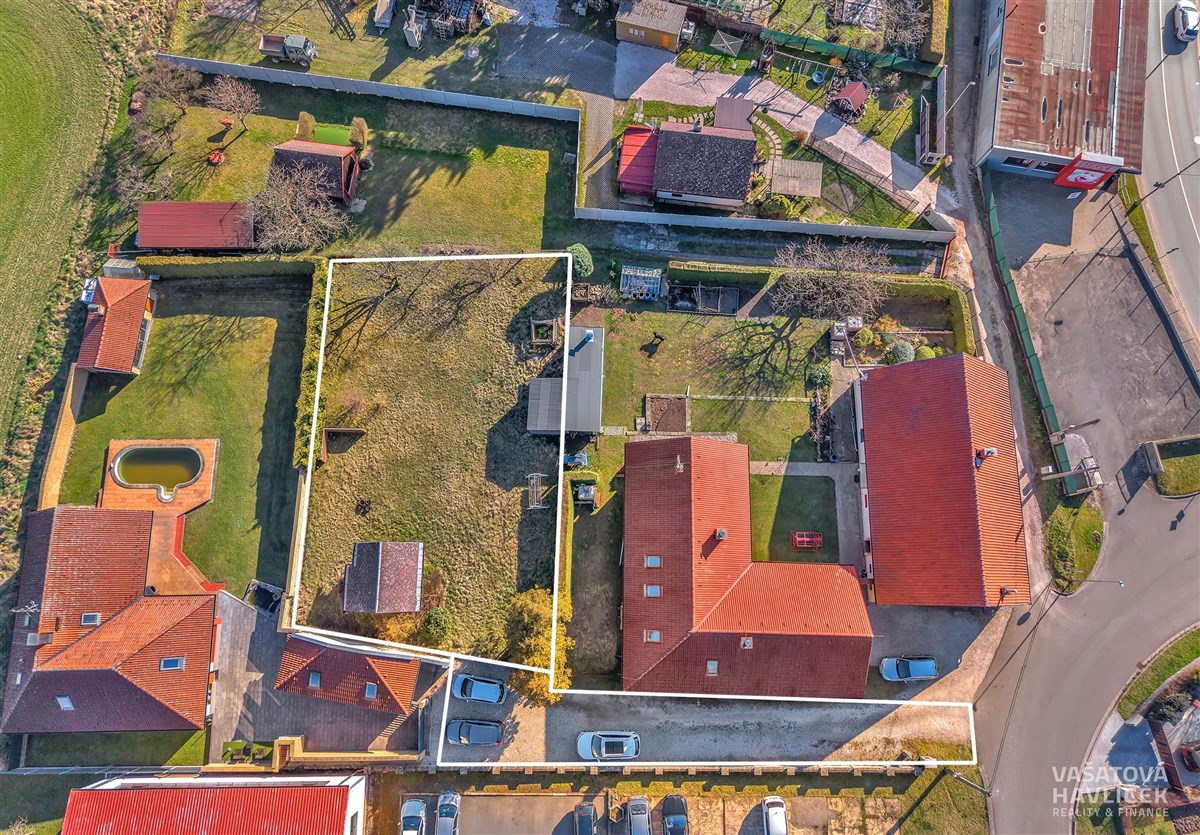 Pozemek s rovinatou travnatou plochou, obklopený plotem, nacházející se v klidné lokalitě s dobrou přístupovou cestou a možností využití pro stavbu domu.