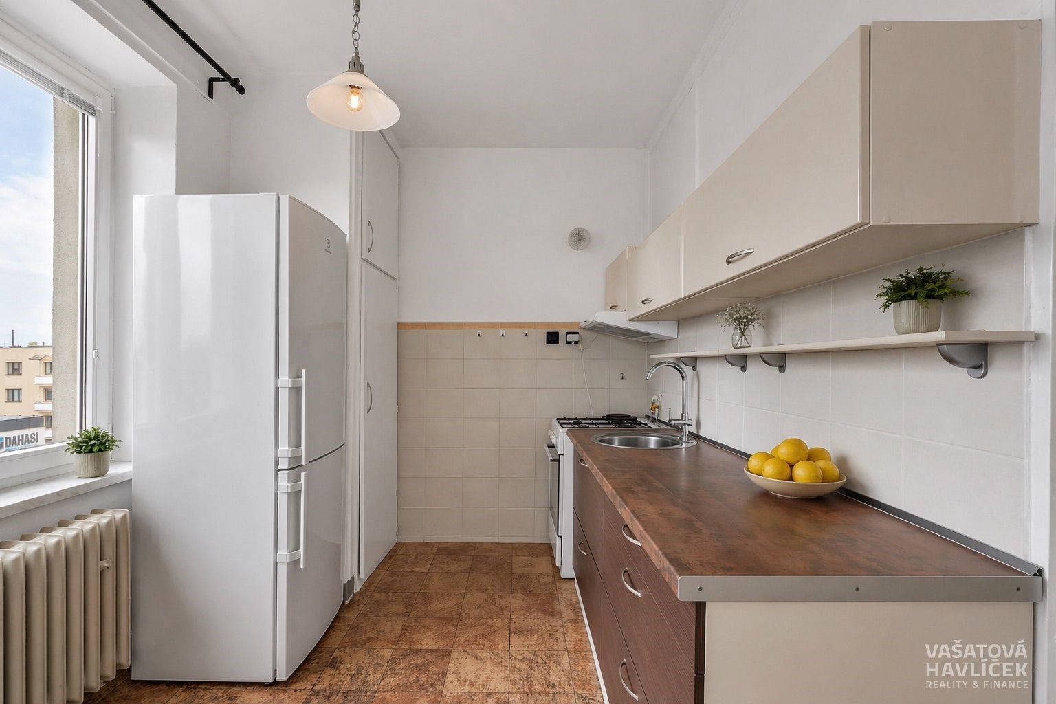 Světlá kuchyň s dřevěnou pracovní deskou, dlažbou a velkým oknem, které zajišťuje dostatek přirozeného světla, moderní spotřebiče a čistý design.