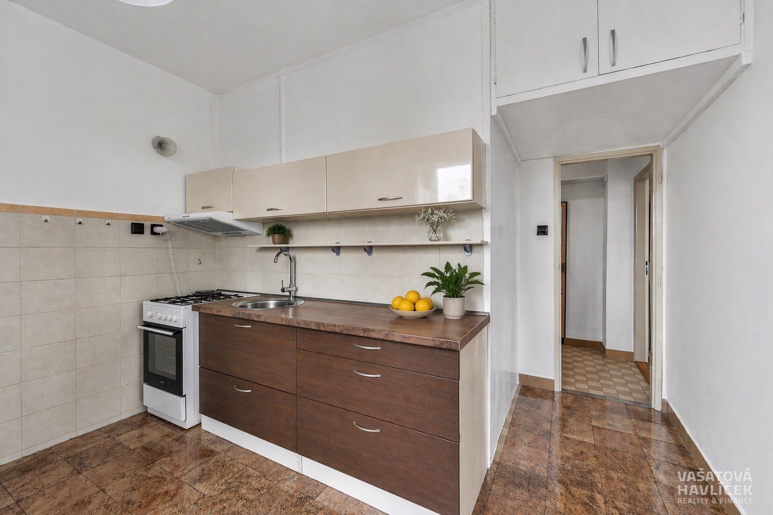 Praktická kuchyň s dřevěnou linkou, světlou dlažbou a vestavěnými skříněmi, ideální pro moderní bydlení.