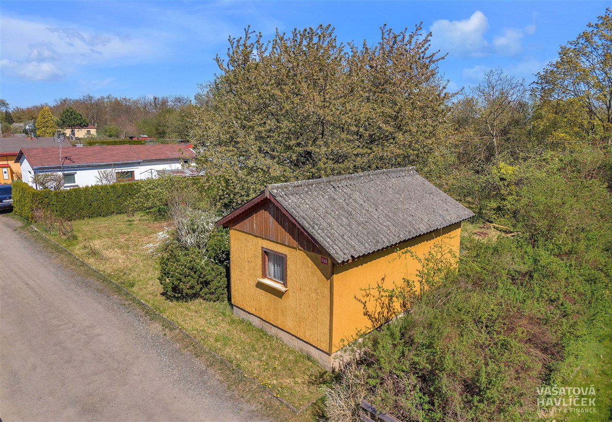 Malá zahradní chatka s žlutou fasádou a sedlovou střechou, obklopená zelení, ideální pro rekreační využití, nachází se v klidné lokalitě.
