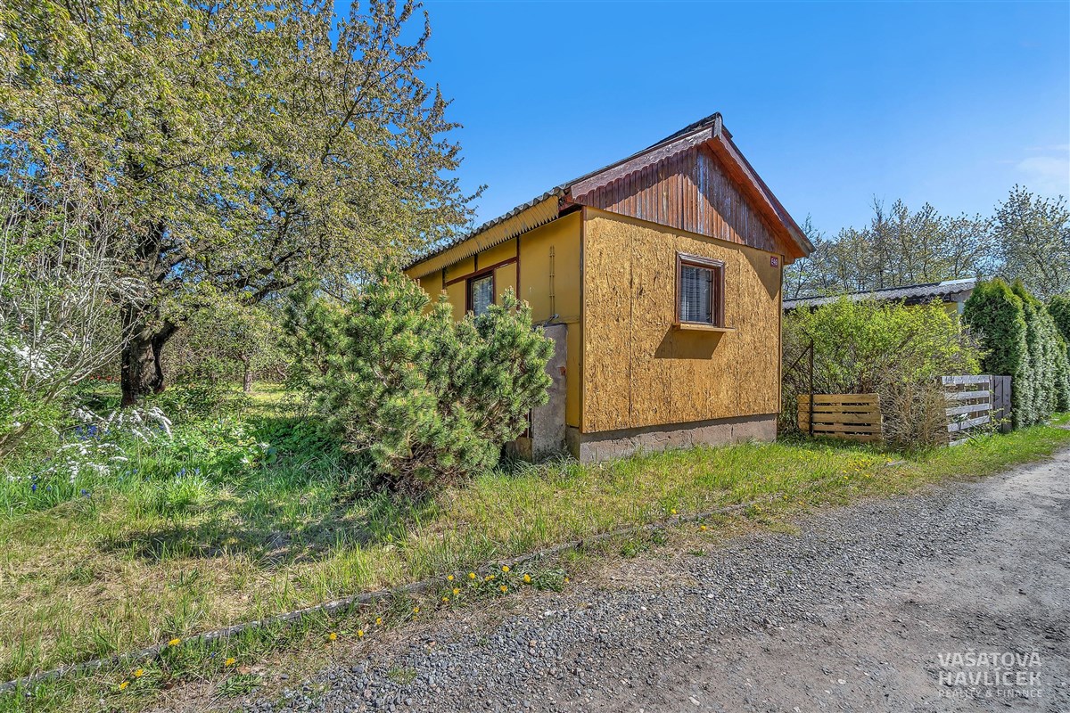 Malý zahradní domek s dřevěným obložením a sedlovou střechou, obklopený zelení, ideální pro rekreační účely nebo zahradničení.