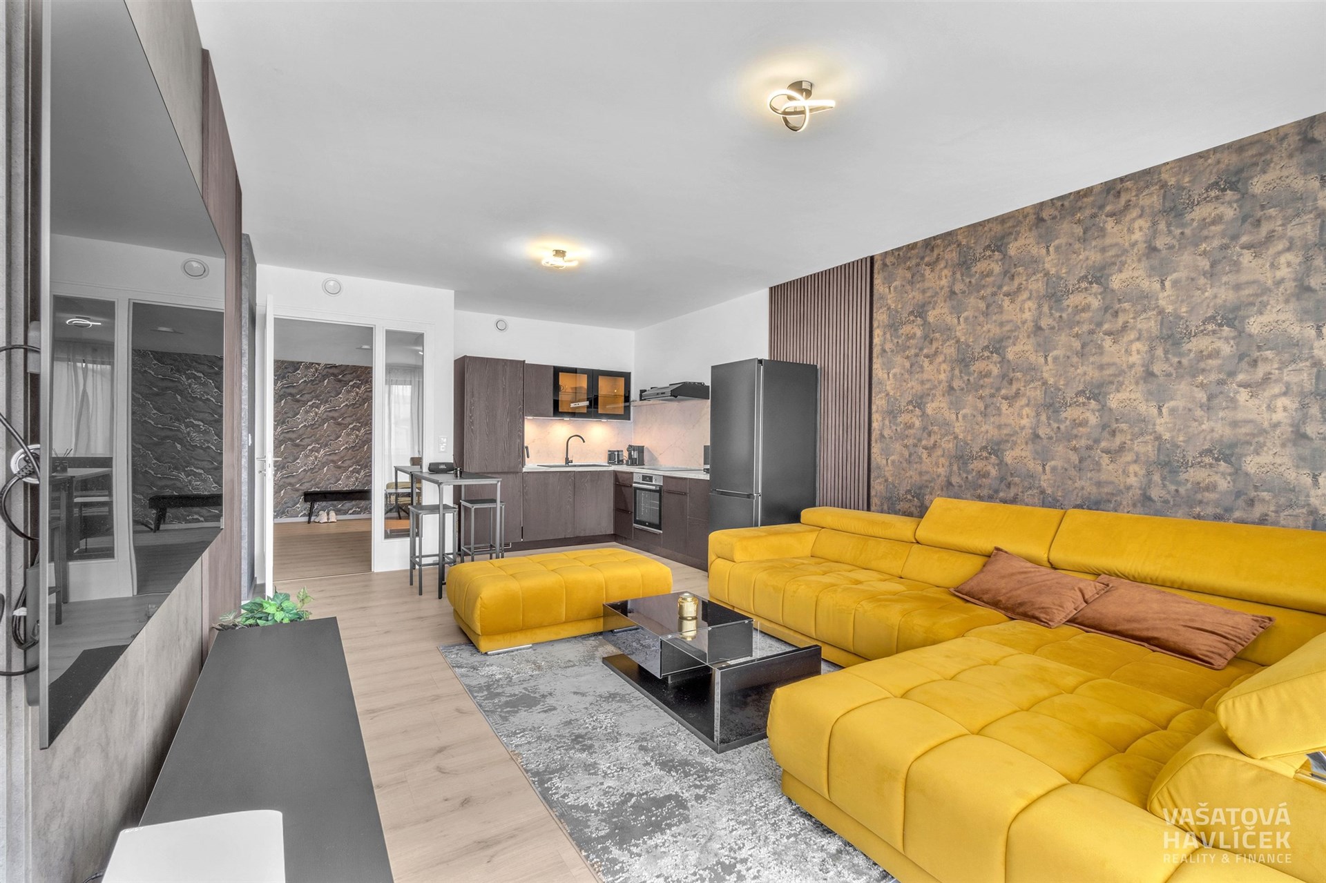 Světlý obývací pokoj s moderní kuchyní, parketová podlaha, velká žlutá sedací souprava, stylový dekorativní obklad, otevřený prostor