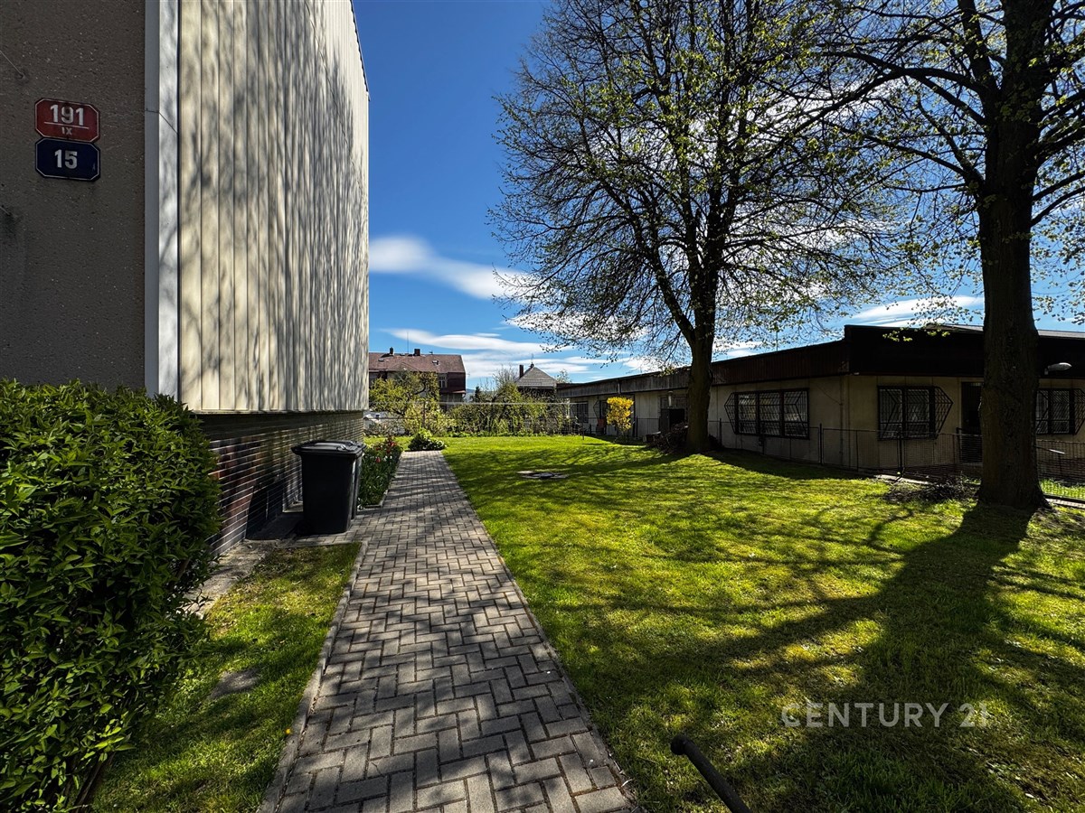 Prázdná zelená zahrada s dlážděnou cestičkou, obklopená stromy, na rovné ploše mezi budovami, nabízí soukromí a klidnou atmosféru.