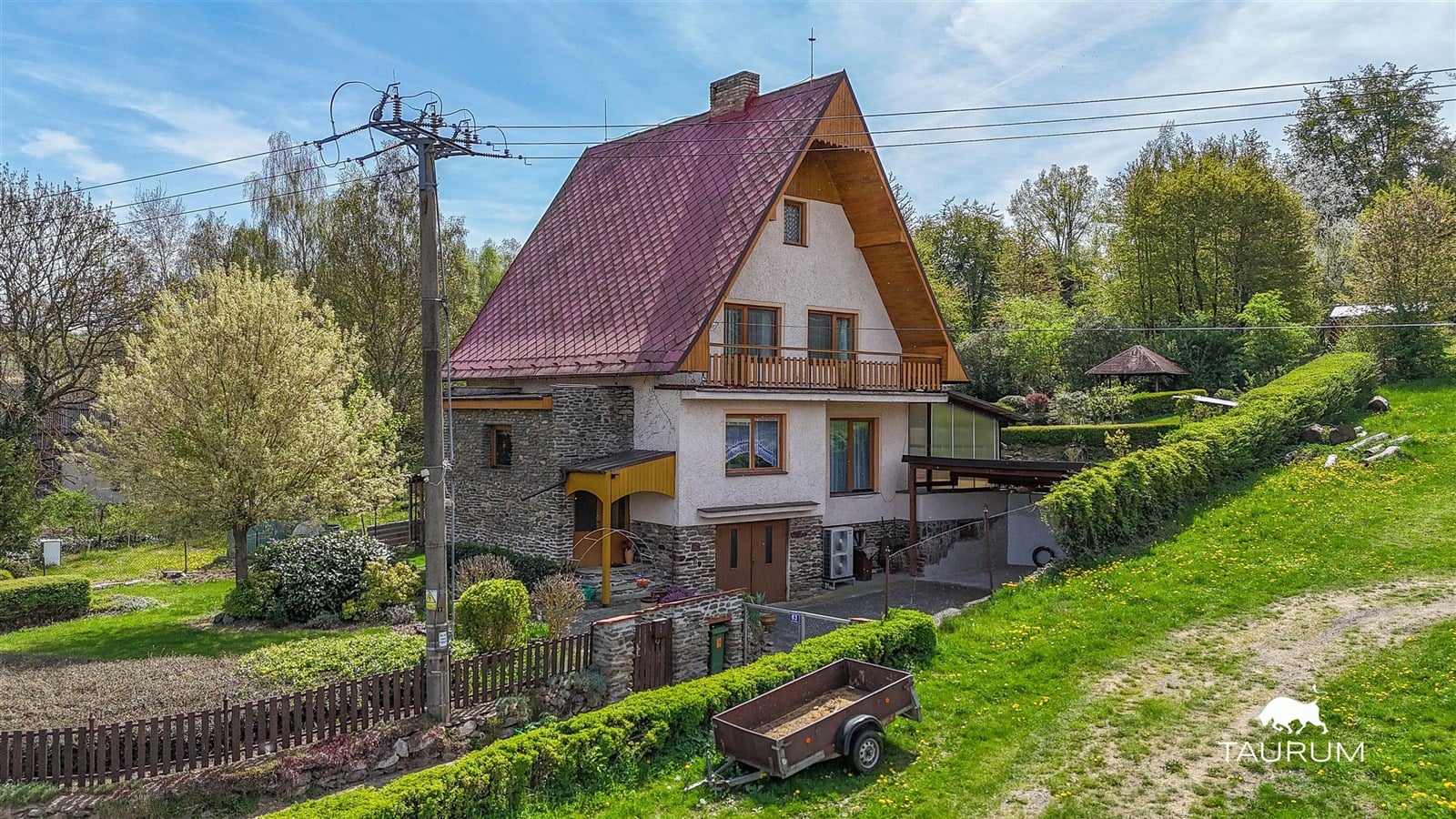 Rodinný dům s kamennými prvky, šikmá střecha, předzahrádka s živým plotem, v klidné lokalitě, obklopený zelení.