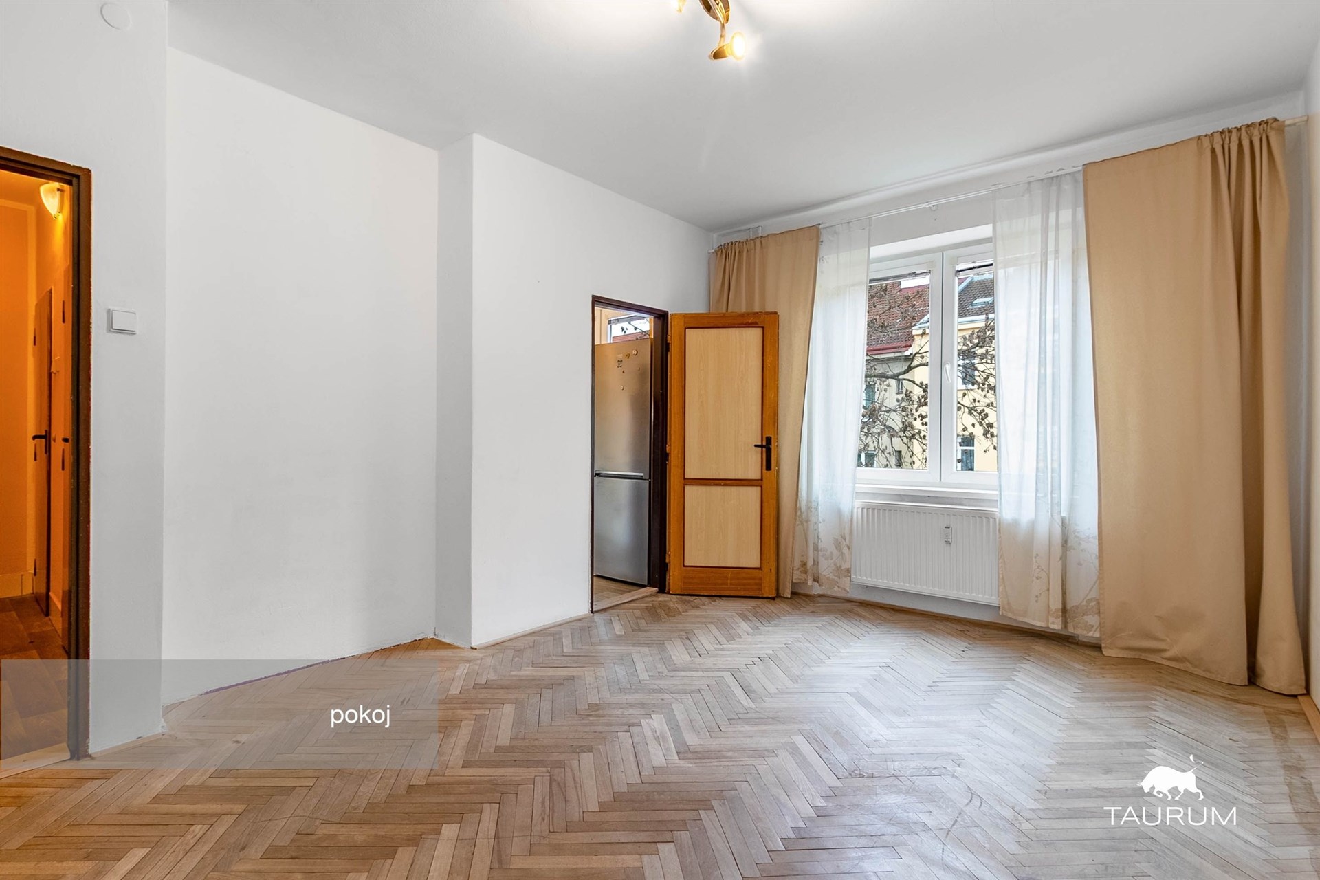 Prostorný pokoj s parketovou podlahou, velkými okny a světlým interiérem, ideální pro moderní bydlení.