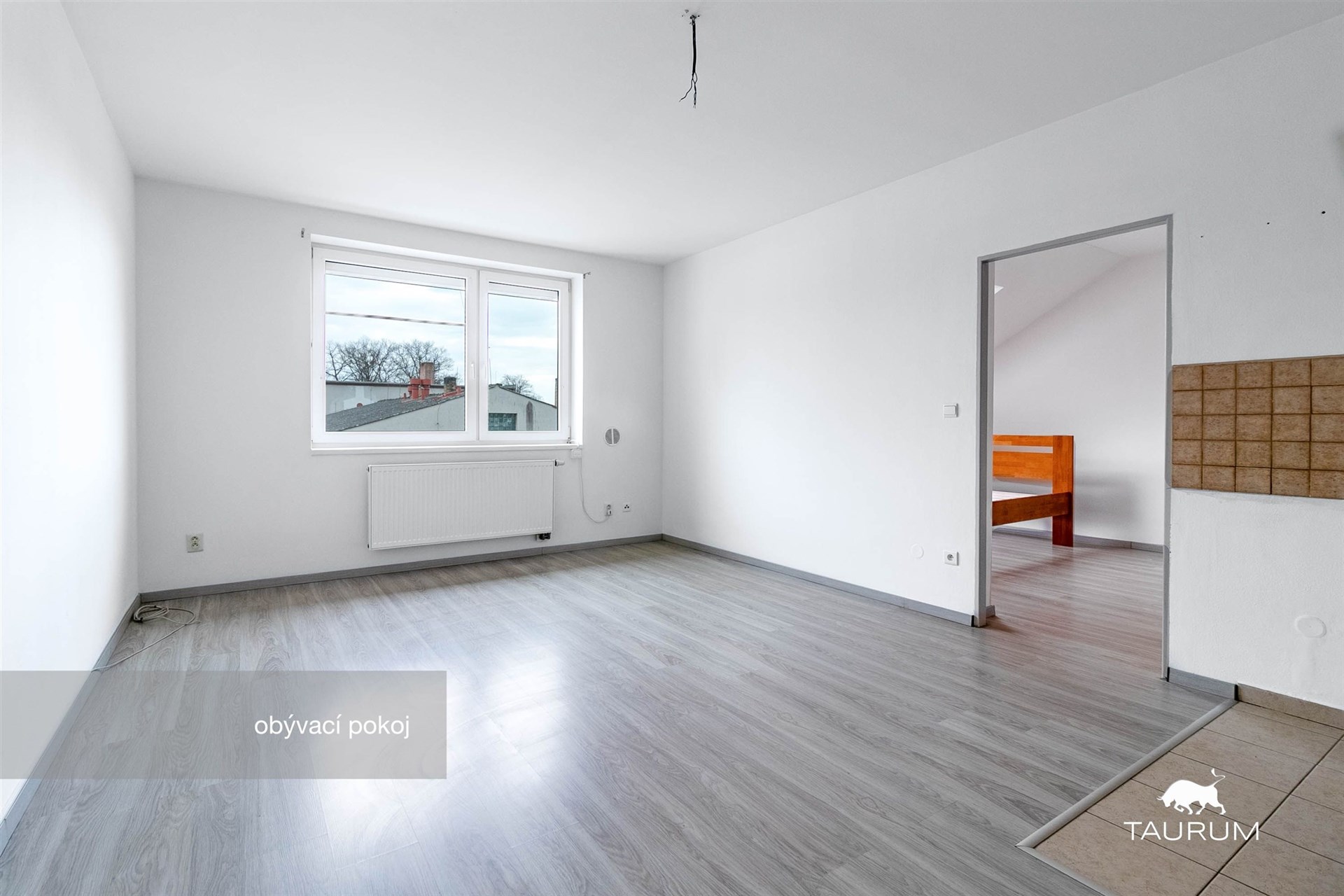 Světlý obývací pokoj s laminátovou podlahou a velkými okny, moderní interiér v rekonstruovaném domě.